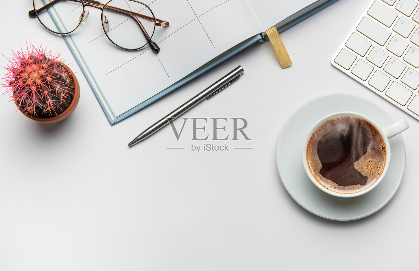 办公桌上有咖啡、仙人掌、钢笔、眼镜和键盘，背景为白色。照片摄影图片
