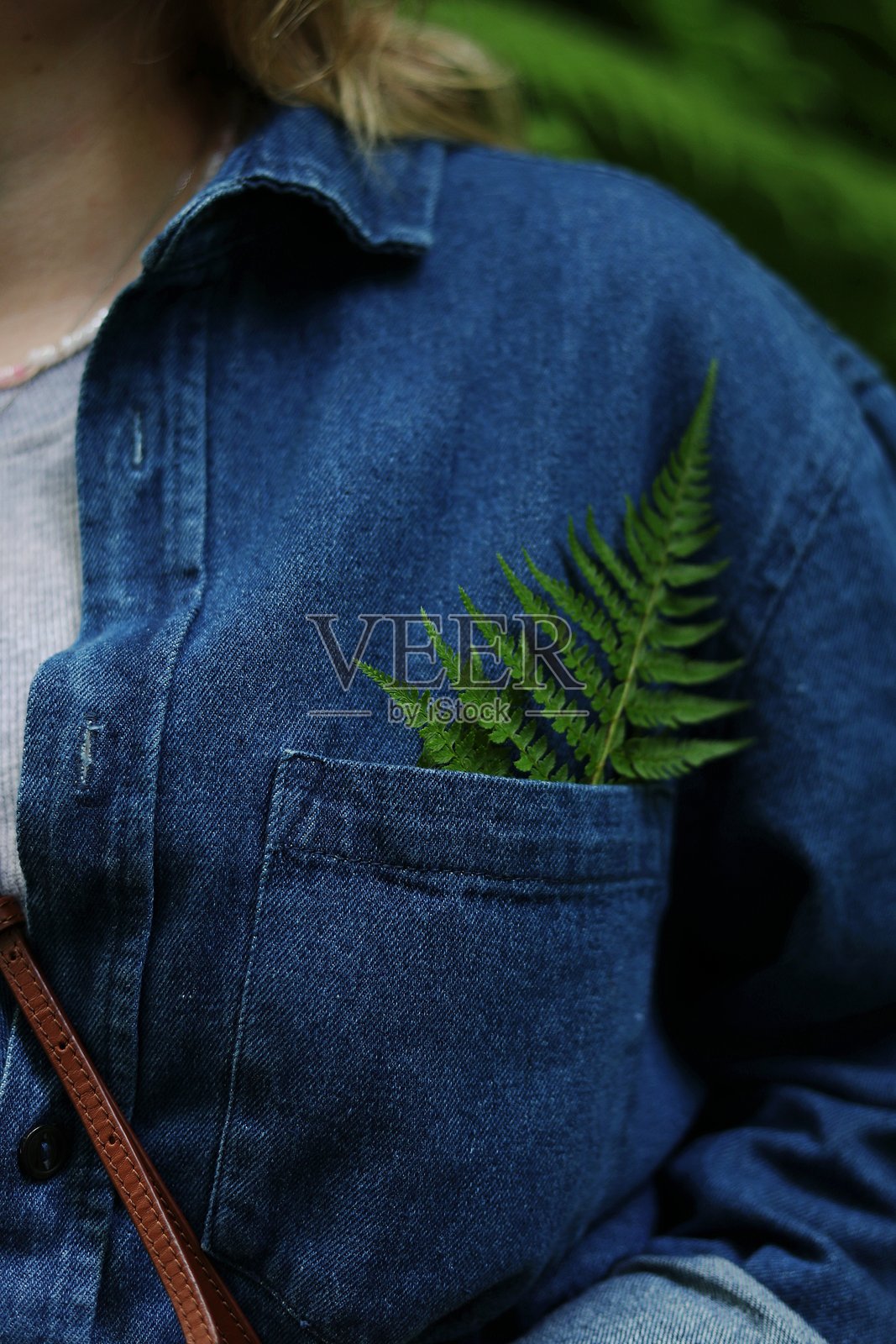 时尚女性的特写，穿着休闲的牛仔服装。胸口口袋里夹着一片绿色蕨类植物，环保。照片摄影图片