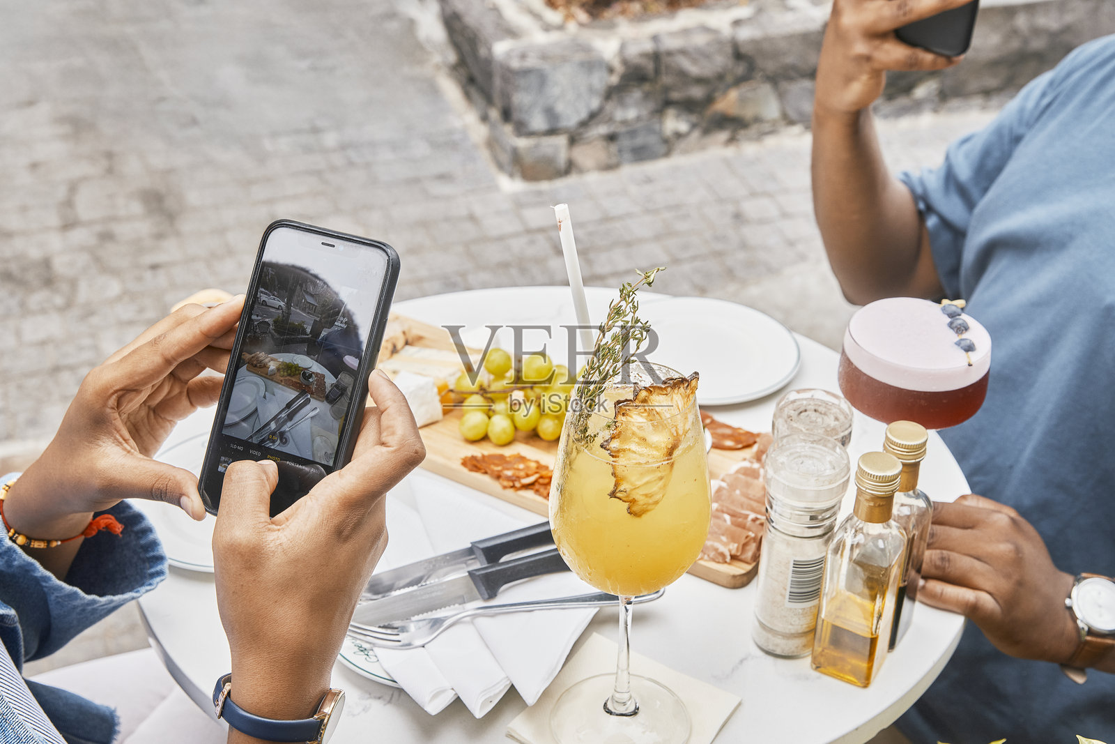 朋友们在街边咖啡馆拍摄冷盘拼盘和开胃酒。男人和女人用手机记录社交媒体时刻，享受周末的放纵，社交、连接，捕捉快乐的回忆以分享在线。照片摄影图片