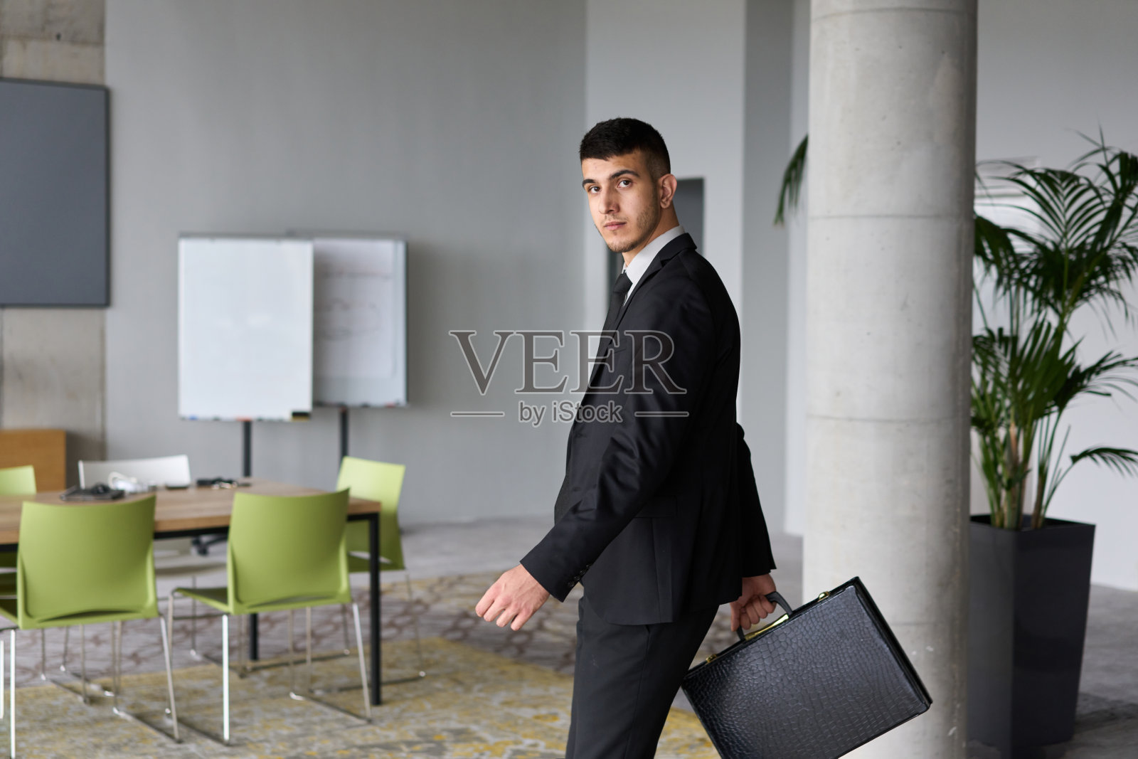一位身穿黑色西装的坚定商人在办公室自信地走着，体现出专业精神和专注，朝着新的挑战迈进。照片摄影图片