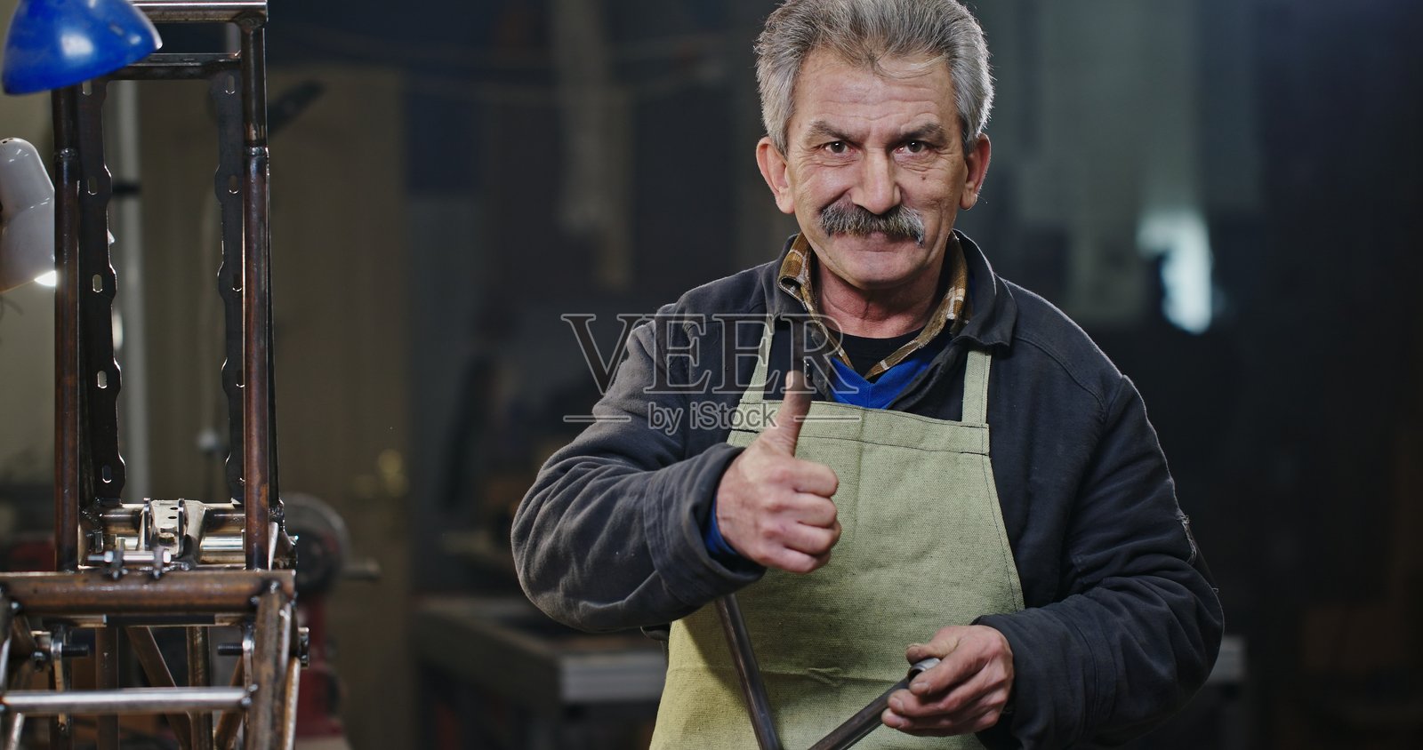 一位熟练的金属工匠在工作坊环境中竖起大拇指。照片摄影图片