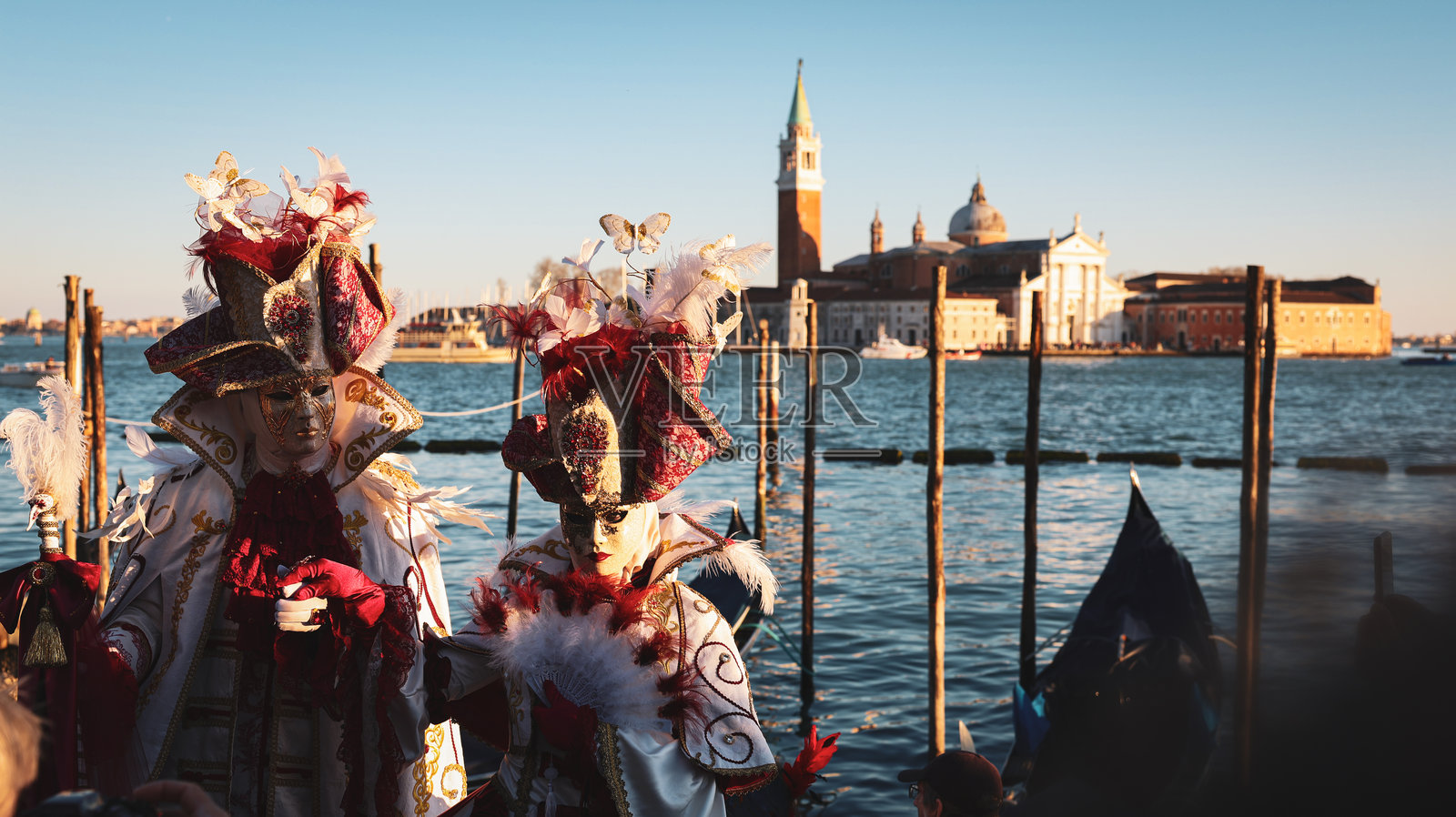 壮丽的威尼斯狂欢节，黄昏时分水边的戴面具人物照片摄影图片