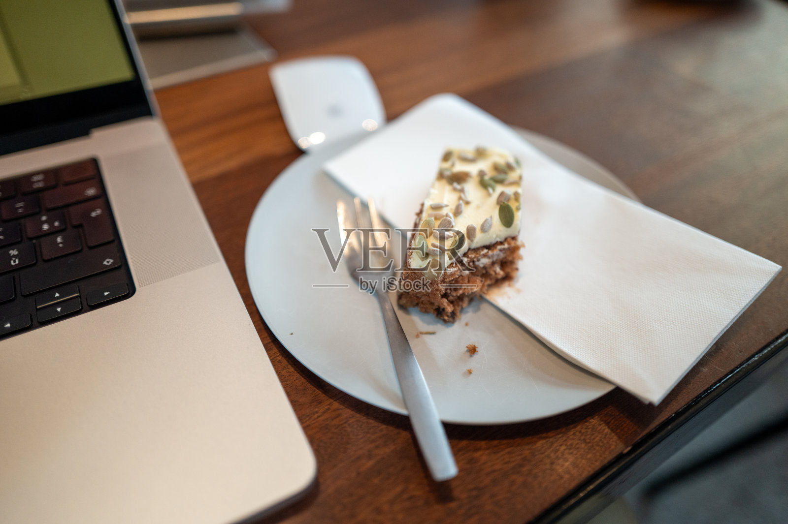 半块吃了一半的南瓜香料蛋糕，配有种子和奶油奶酪糖霜，放在木桌上的笔记本电脑旁边照片摄影图片