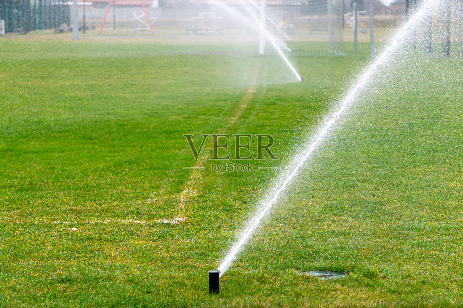 花园喷灌器向草坪喷洒水。干旱期间的草坪灌溉系统。在炎热的日子里喷洒水雾。照片摄影图片