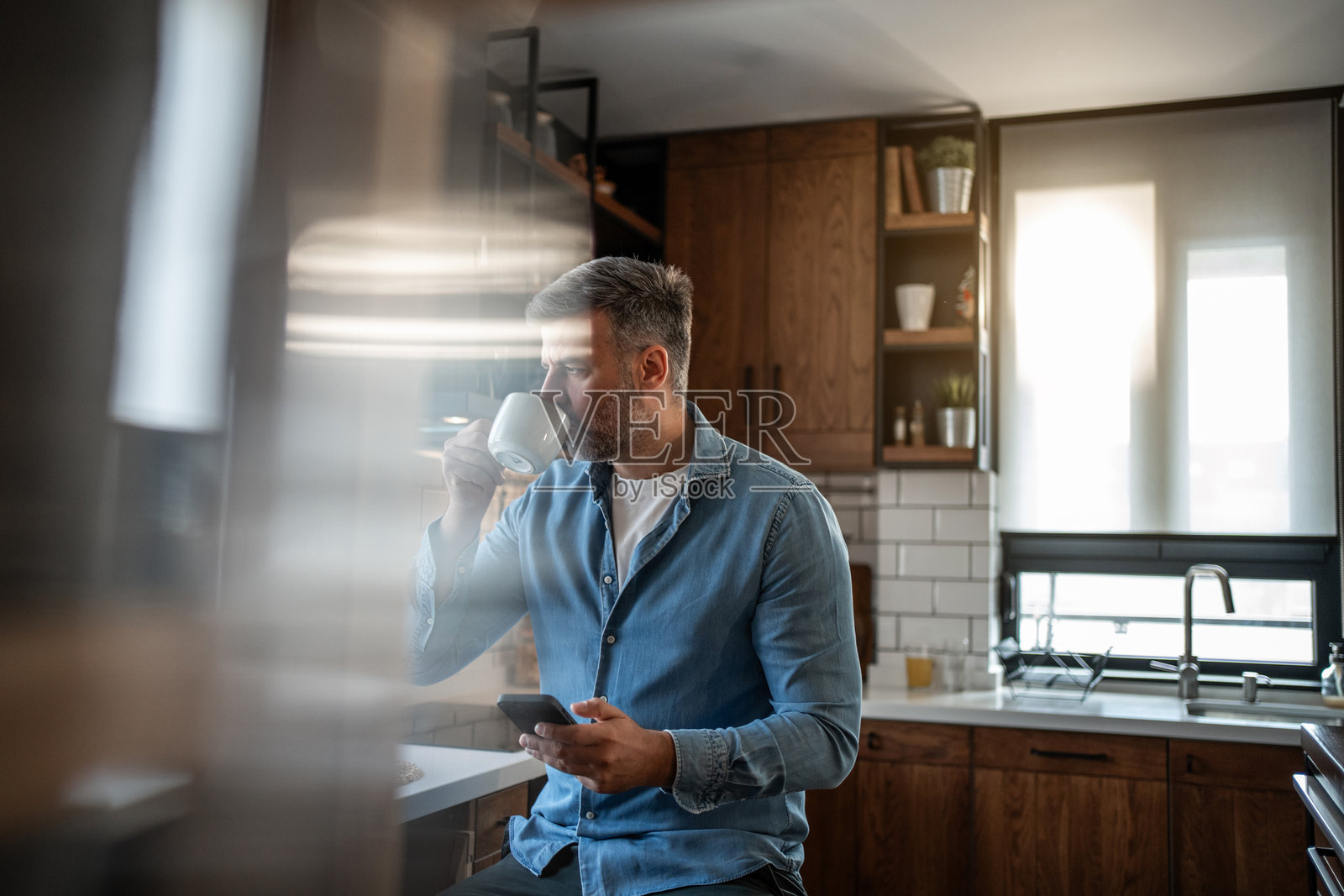 中年男子在厨房喝咖啡并使用智能手机照片摄影图片