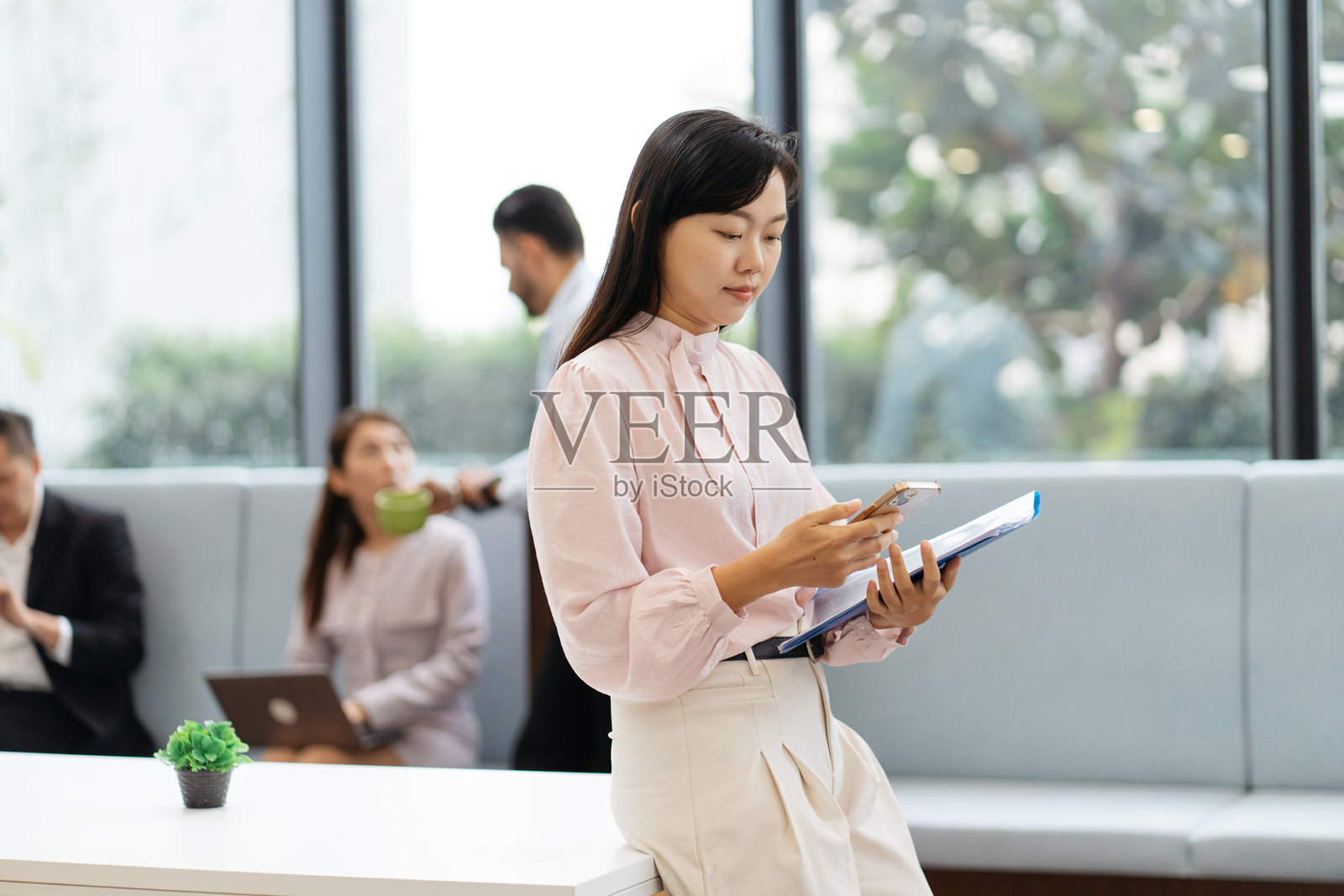 亚洲女商人在现代办公室里手持文件并使用智能手机工作照片摄影图片