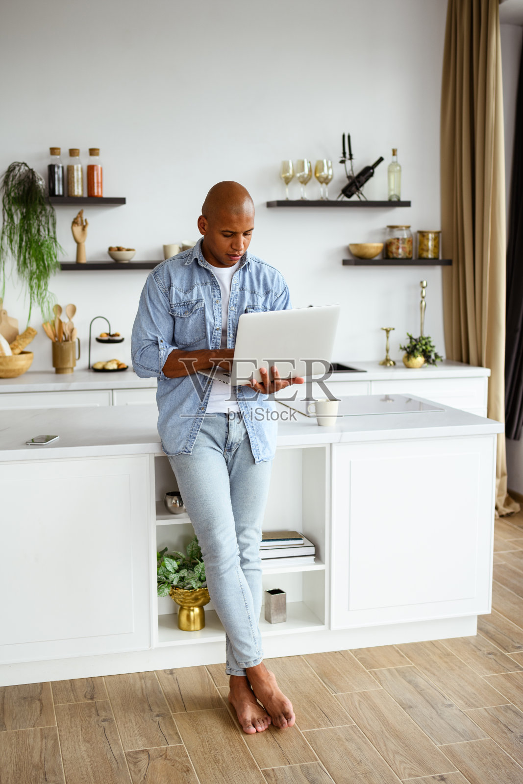 赤脚的非裔美国自由职业者在现代厨房中使用笔记本电脑照片摄影图片