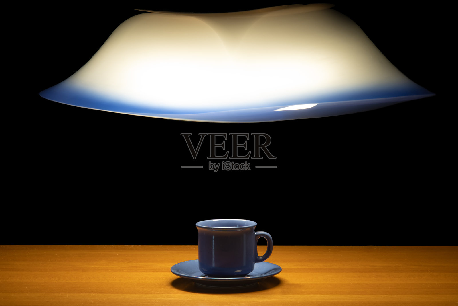 一只茶杯放在桌子上，灯光下的移动吊灯照耀着，背景为黑色。照片摄影图片