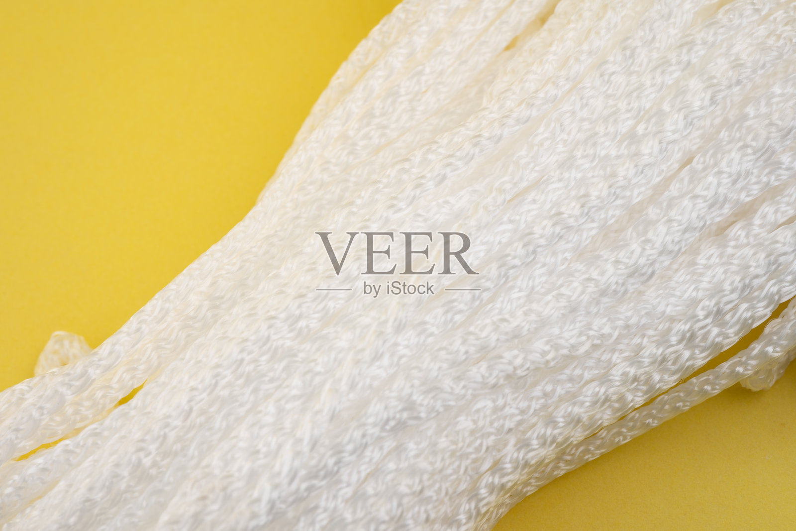 白色编织材料放在明亮的黄色表面上，展示出独特的纹理和细节，沐浴在自然光下。照片摄影图片