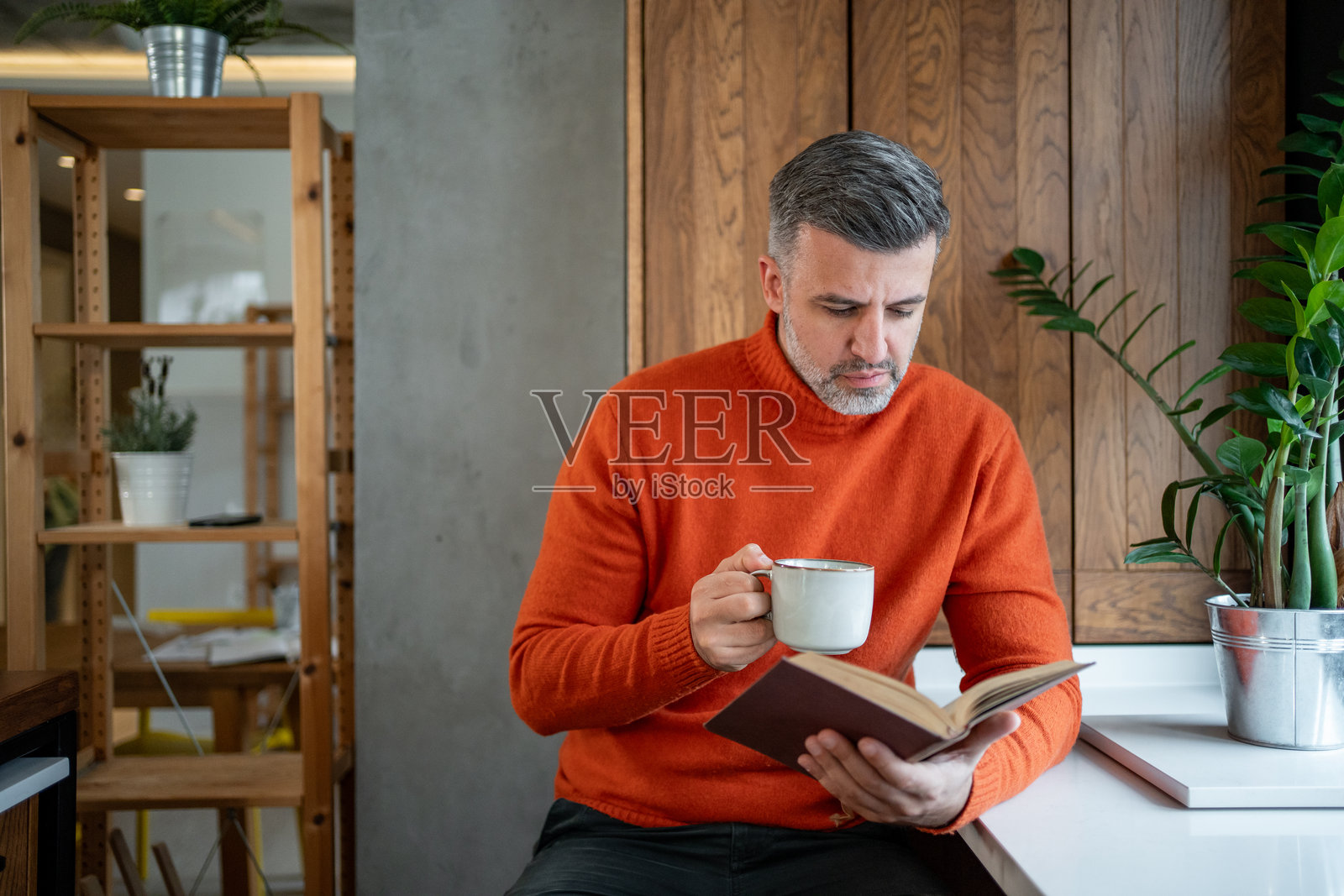 成熟男性在现代厨房里阅读一本书并喝咖啡照片摄影图片