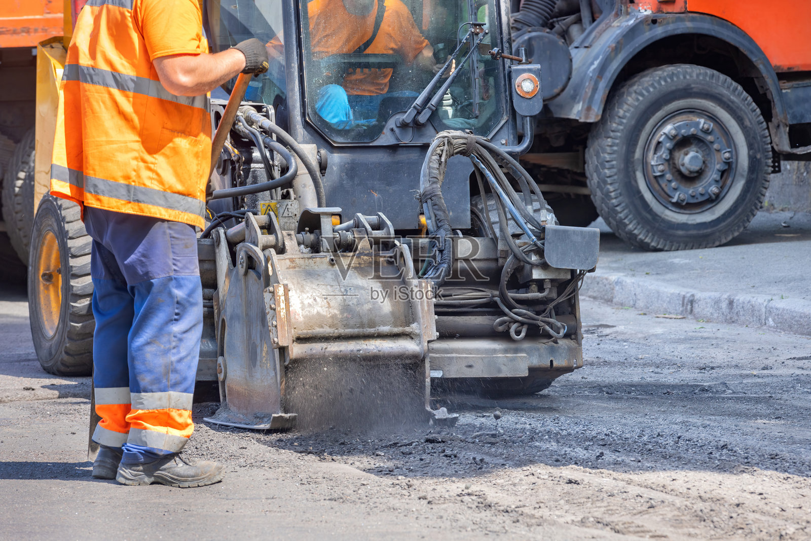 一名穿着橙色安全背心的建筑工人认真操作一台紧凑型道路修复机。照片摄影图片
