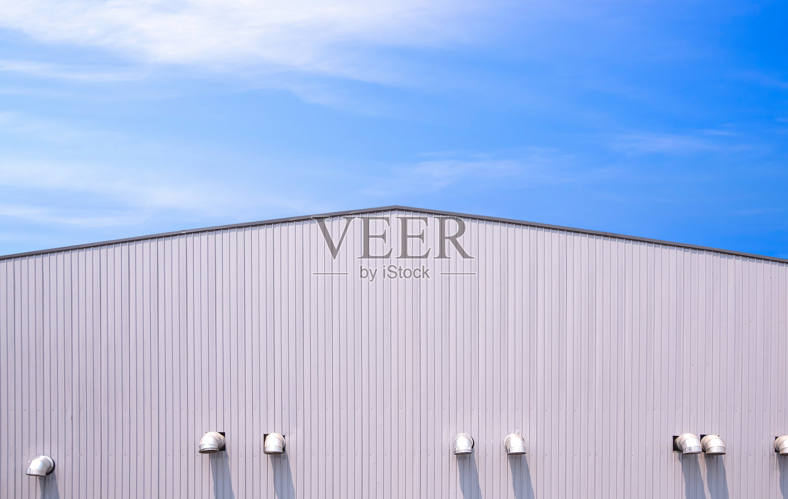 大型工厂工业生产建筑，铝制波纹钢墙和山形屋顶上有通风空气管道，背景是蓝天。照片摄影图片