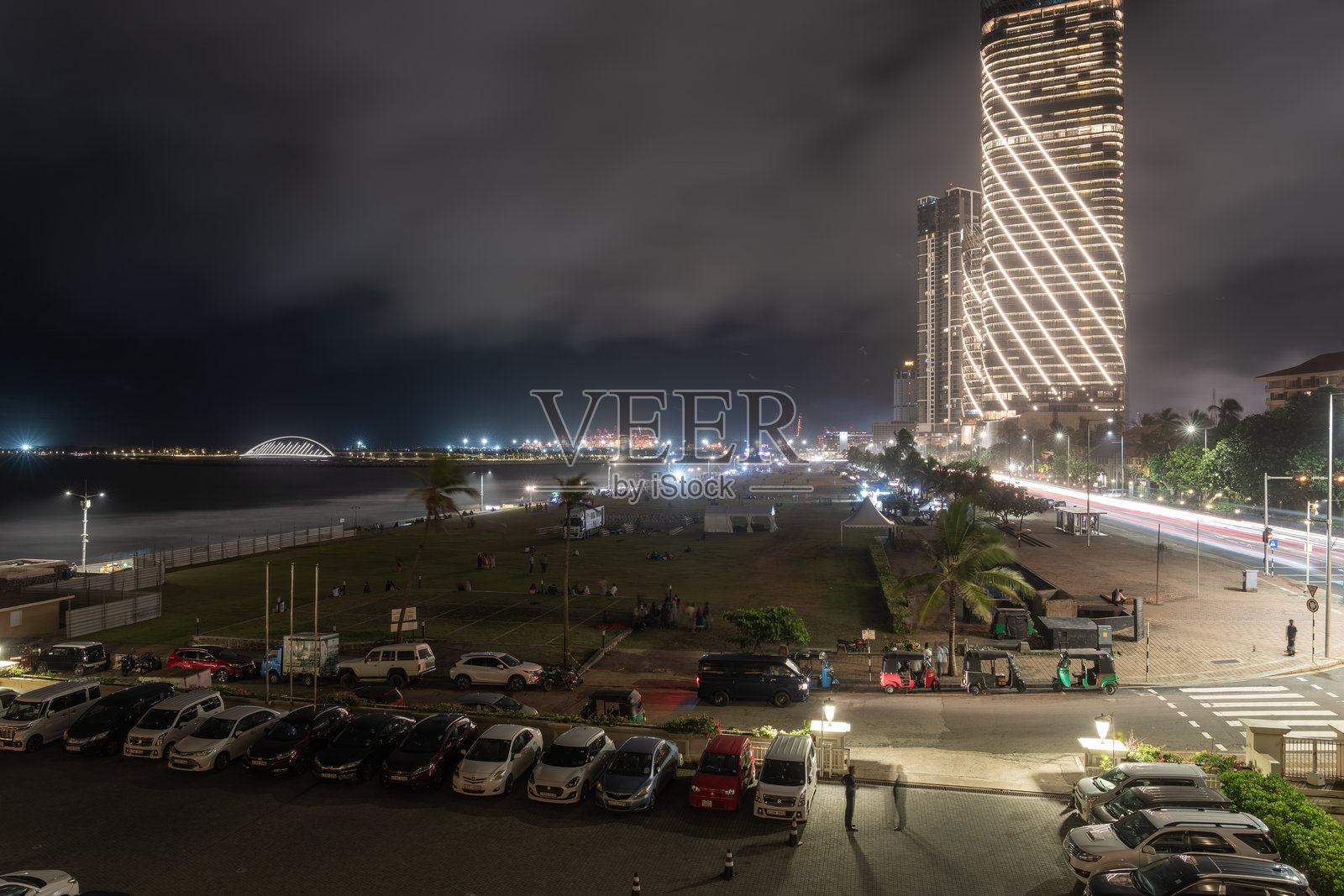 加勒面绿地的夜景，停放的汽车和远处现代高层商业建筑的港口设施。照片摄影图片