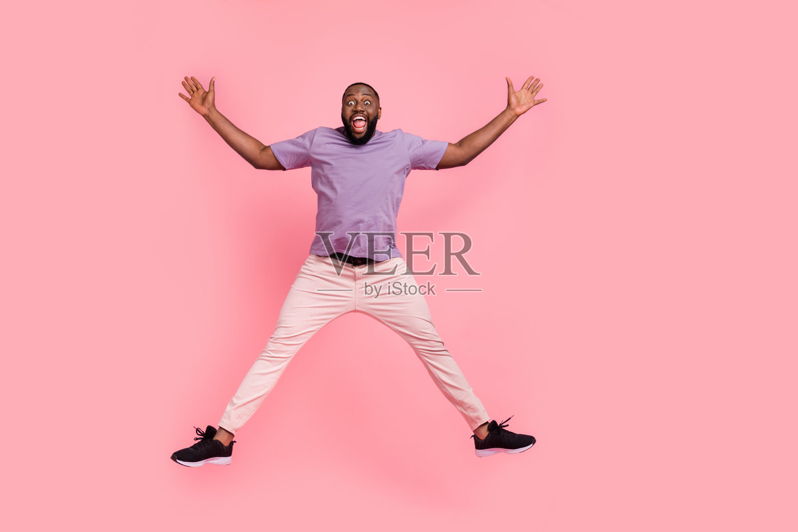 全身身材的迷人快乐男孩在粉色柔和背景上跳跃嬉戏照片摄影图片