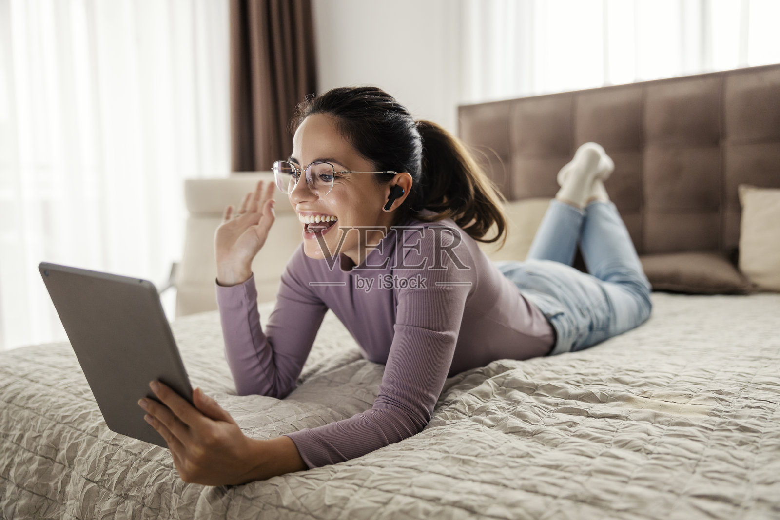 愉快的女人躺在卧室的床上进行视频通话。照片摄影图片