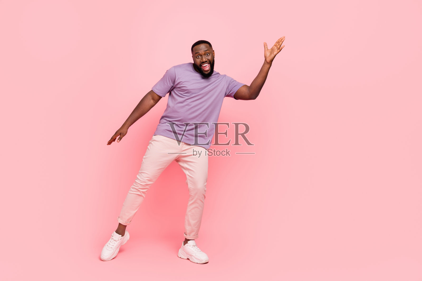 穿着紫色T恤的兴奋搞笑男孩在粉色背景下微笑跳舞照片摄影图片