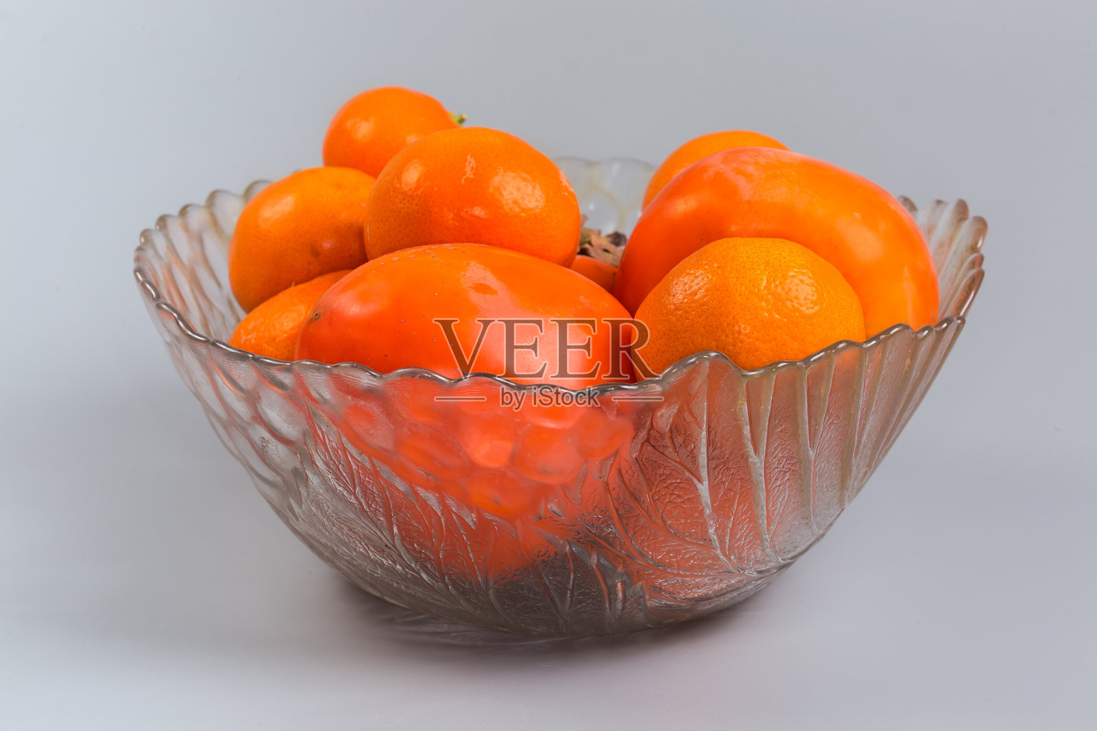 灰色背景上的玻璃水果碗里装着柿子和橘子照片摄影图片