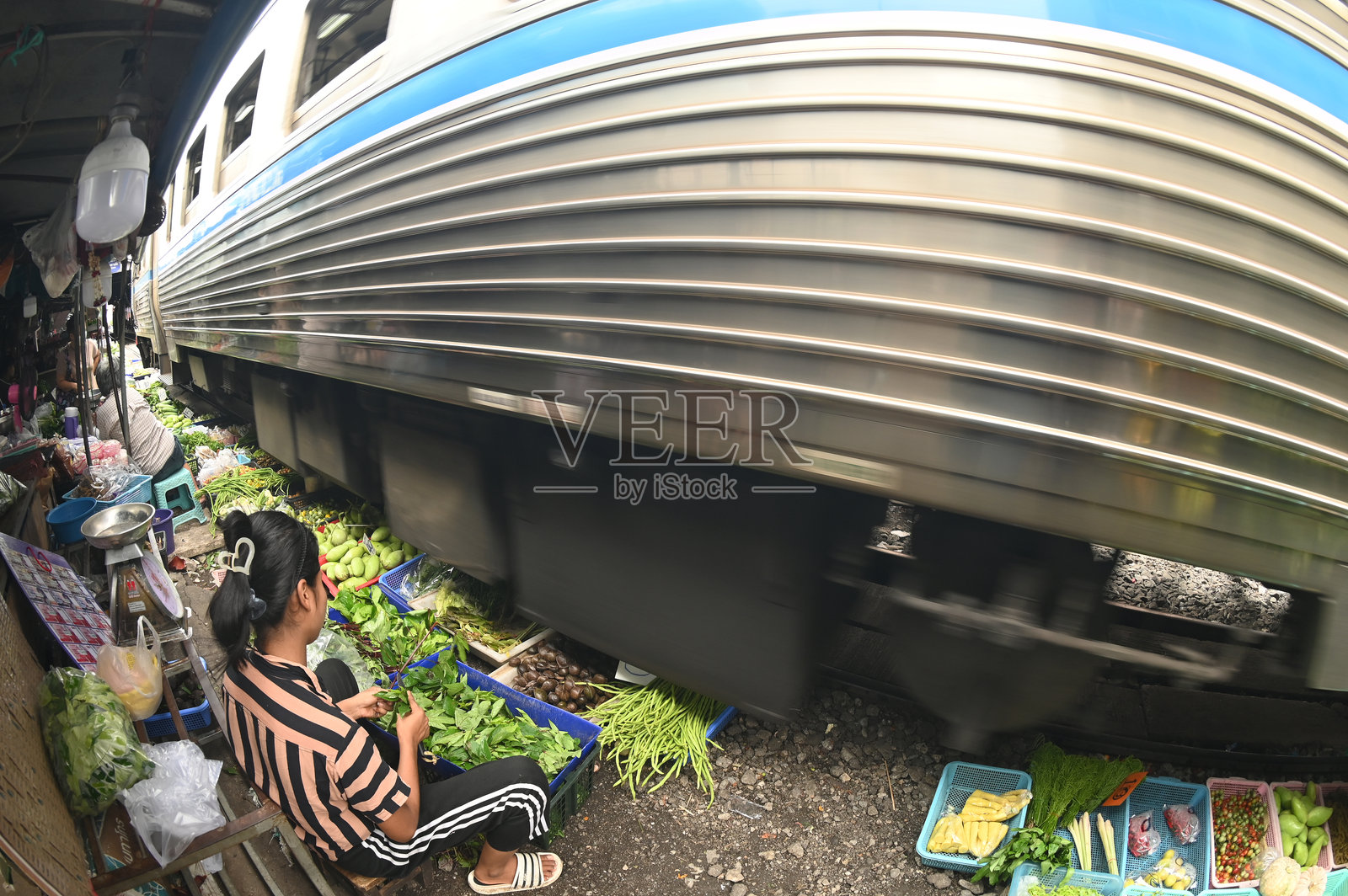 在马哈柴车站,摊贩沿着铁路出售蔬菜、水果和鲜花。当火车到来时,她会保持货架不动,因为它们较低。照片摄影图片