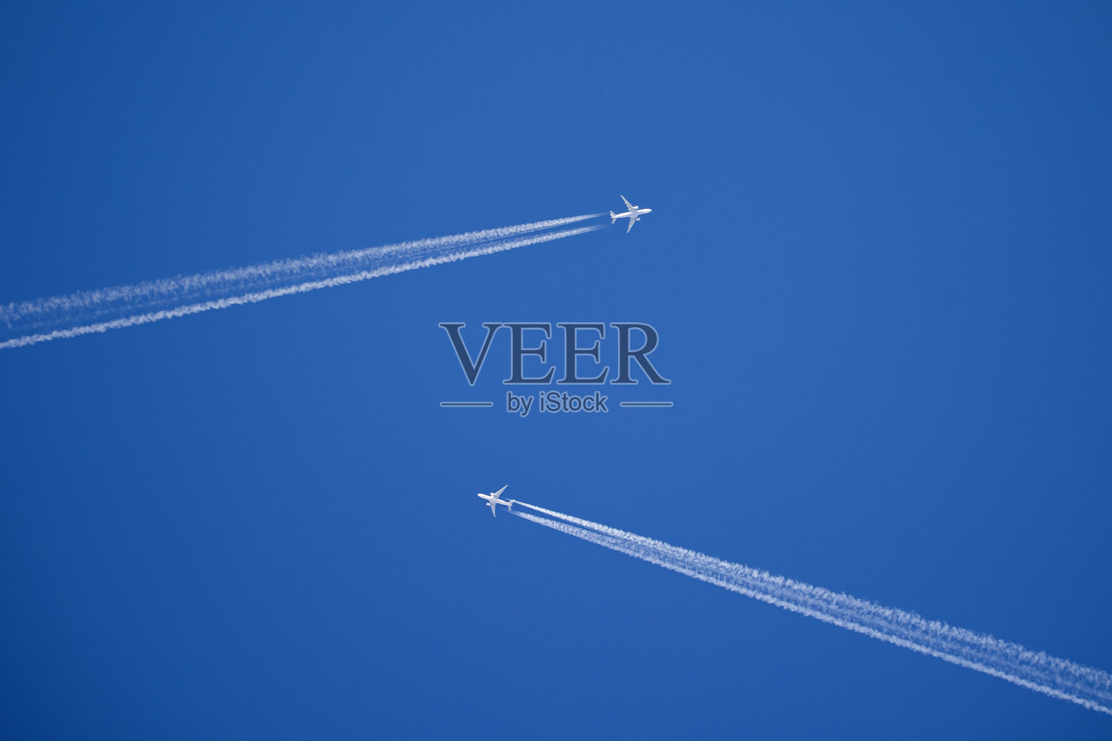 两架白色喷气机在蓝天中相向飞行，前方留有长长的尾迹。照片摄影图片