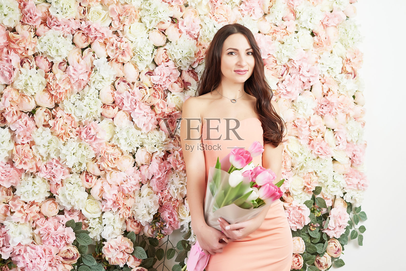 手握郁金香花朵的美丽女孩，背景是花卉图案。适合3月8日国际妇女节或母亲节的贺卡。非常漂亮的花艺师手捧色彩斑斓的盛开花束。照片摄影图片