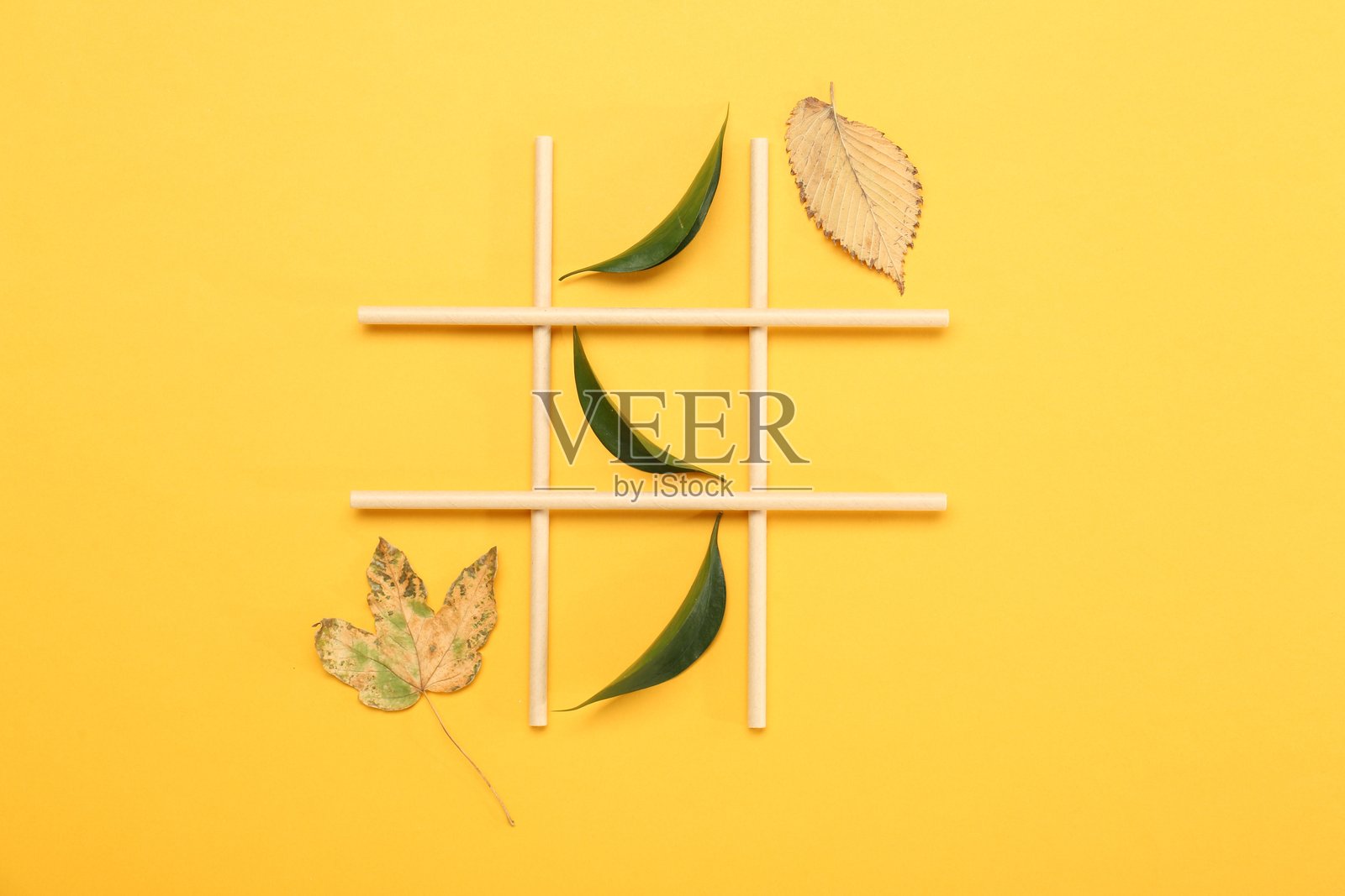 用新鲜和干燥的叶子在黄色背景上制作的井字游戏，俯视图照片摄影图片