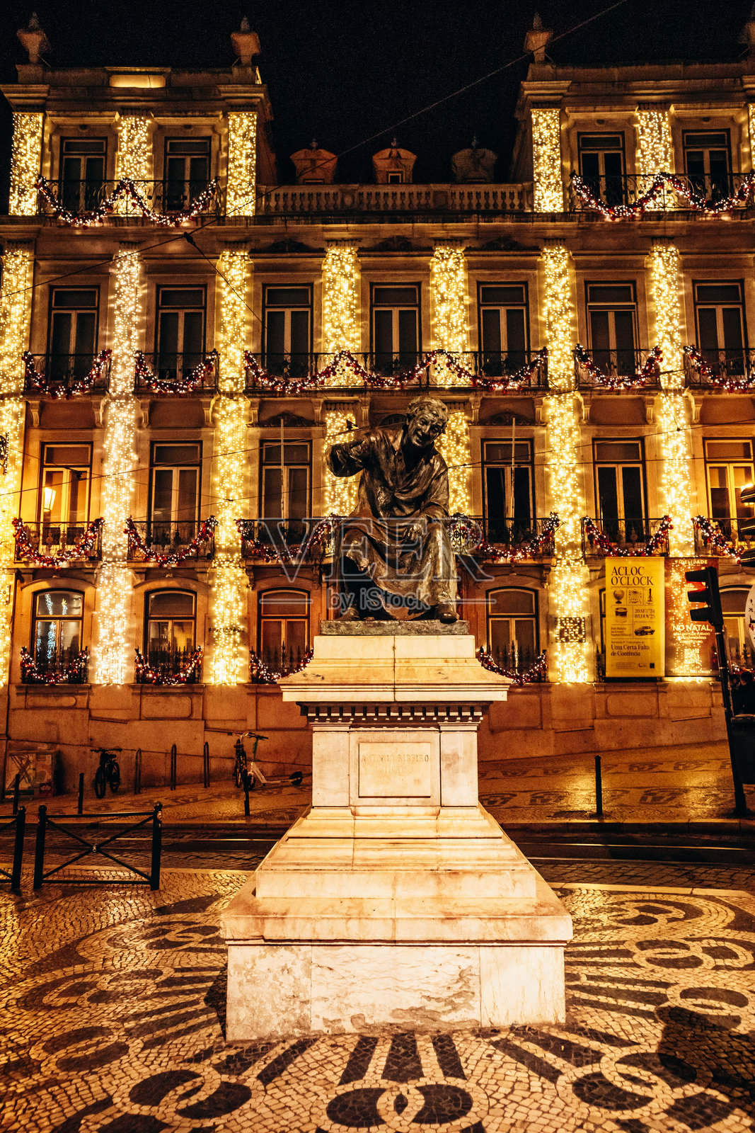 安东尼奥·里贝罗的雕像被装饰在附近建筑上的节日灯光照亮，鹅卵石街道为广场增添了魅力。照片摄影图片
