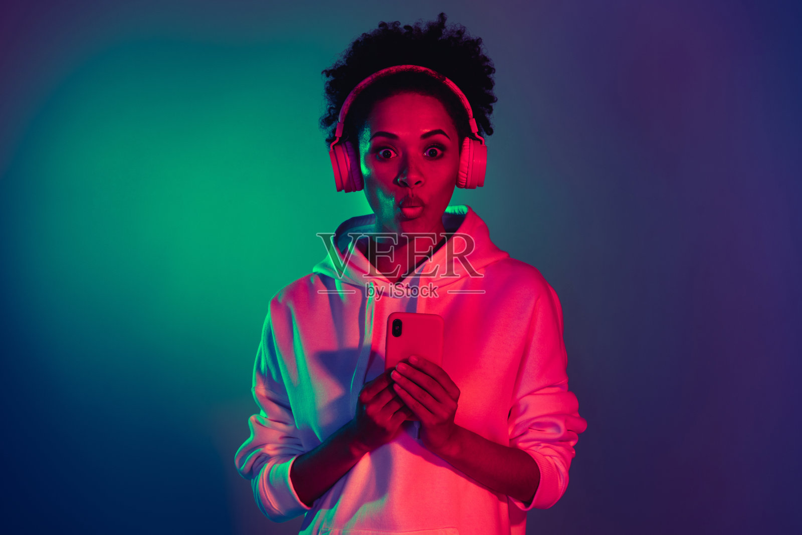 迷人的时尚女孩在明亮的多彩渐变背景下，惊讶地听着旋律，撅着嘴唇。照片摄影图片