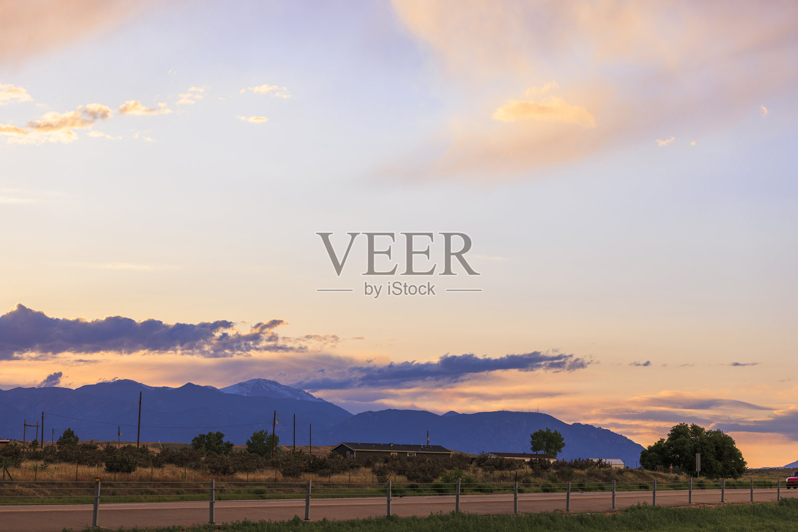 云彩在科罗拉多山峰上捕捉到金色的光芒。乡村风景延绵，围栏田野和远处的房屋交错。照片摄影图片