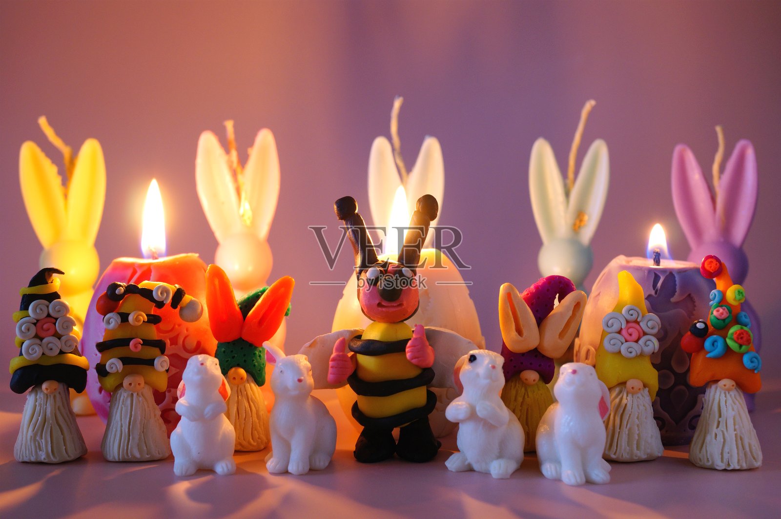 一只蜜蜂雕像、侏儒和玩具兔子在复活节蜡烛的背景下。照片摄影图片