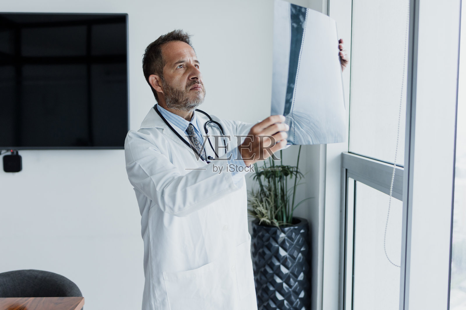 墨西哥拉丁美洲办公室或医院里，一位年长的拉丁裔男性医生专家正在查看X光扫描。照片摄影图片