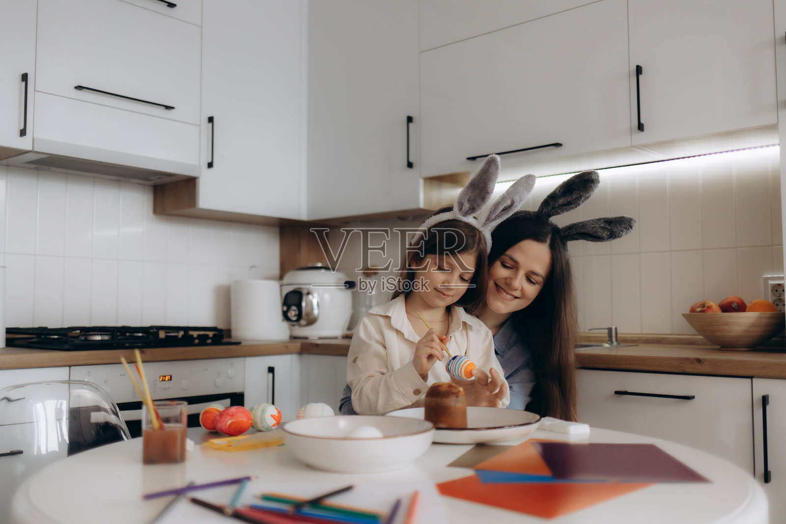 母亲和女儿在厨房里一起戴着兔耳朵绘制复活节彩蛋照片摄影图片