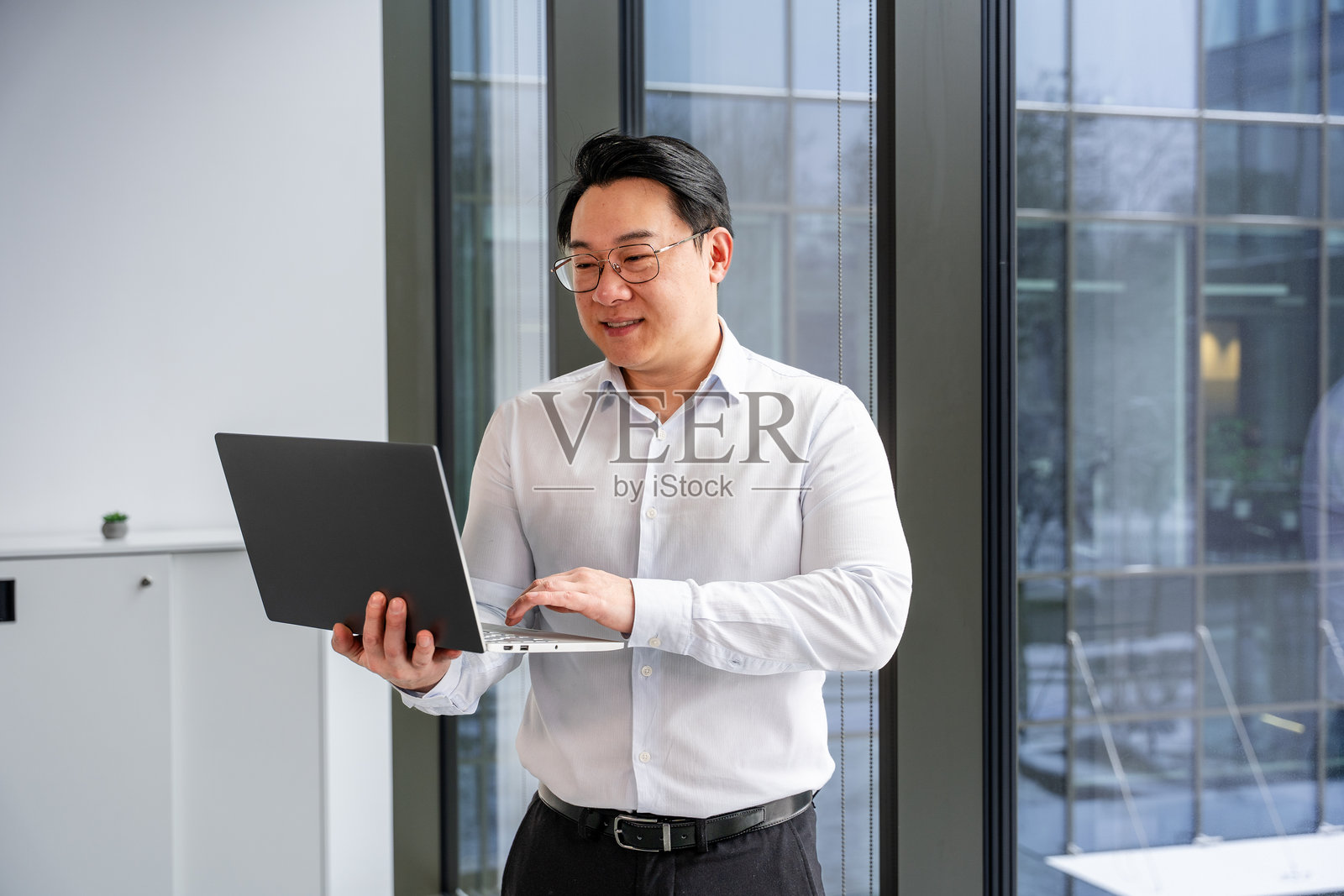 现代办公室内使用笔记本电脑的专业商务人士，玻璃内饰设计。照片摄影图片