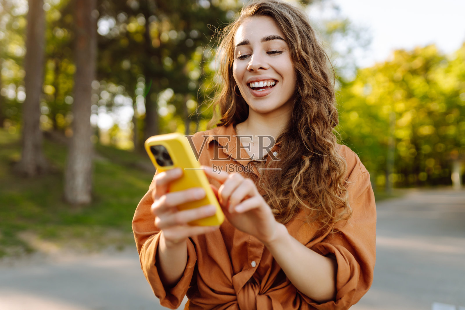 年轻女性手持手机在公园散步的肖像。照片摄影图片