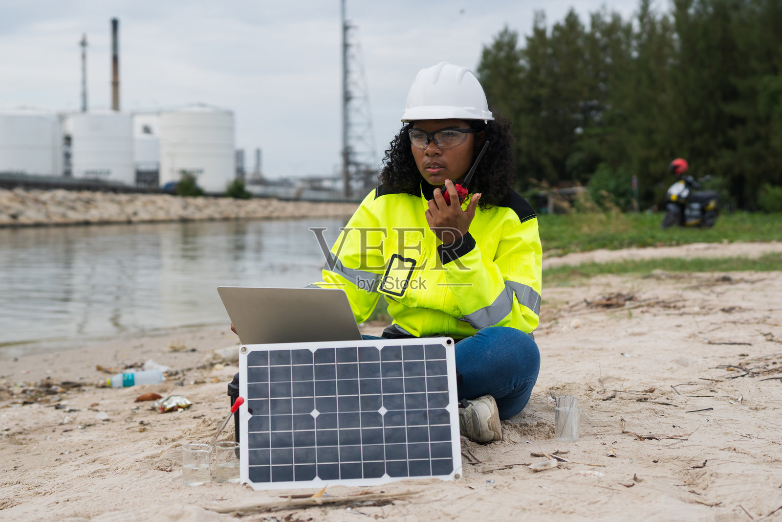 女性工程师在石油炼油厂和天然气炼油厂使用对讲机和笔记本电脑检查生产质量和安全。照片摄影图片