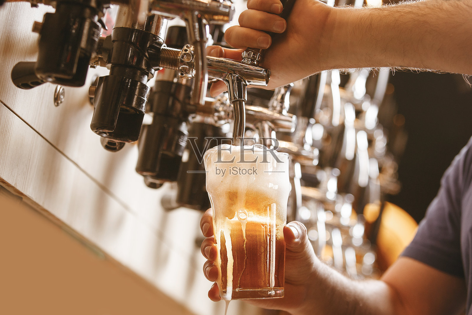 男子在酒吧从龙头倒入冰镇啤酒到杯子里照片摄影图片