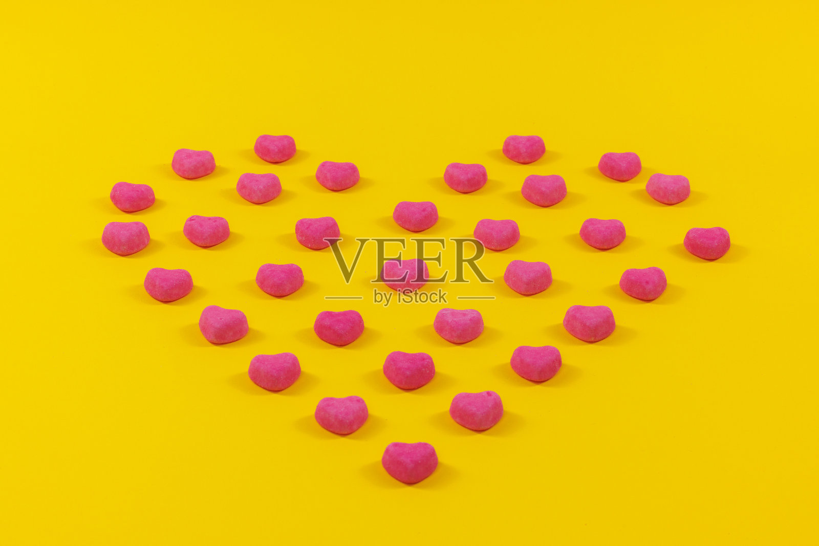 多彩糖果在黄色背景上呈心形条纹排列照片摄影图片