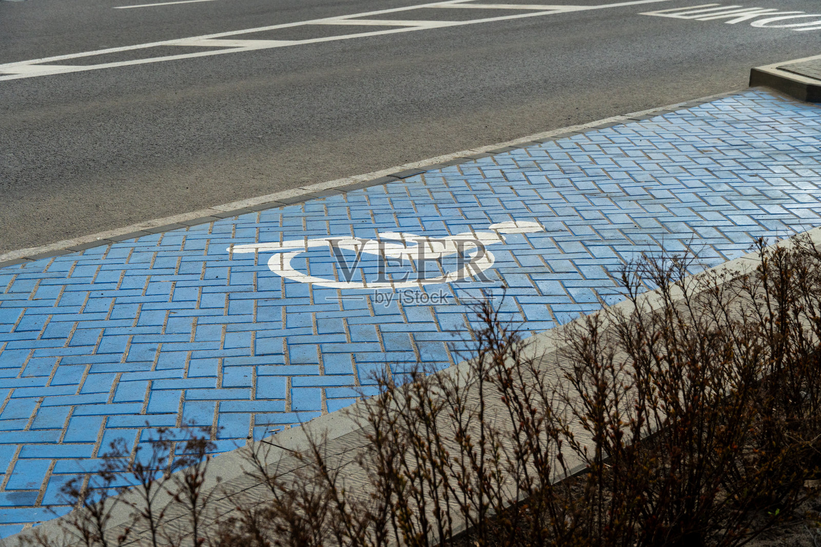在城市道路旁的蓝色铺砌人行道上标记了一个无障碍停车位，方便残疾人士在白天使用。照片摄影图片