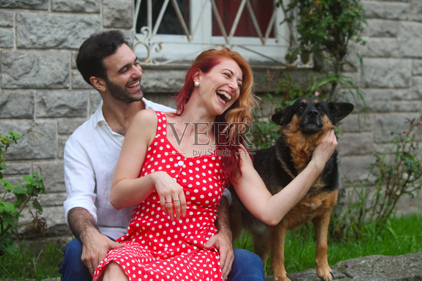 快乐的情侣与他们的狗坐在家旁边照片摄影图片