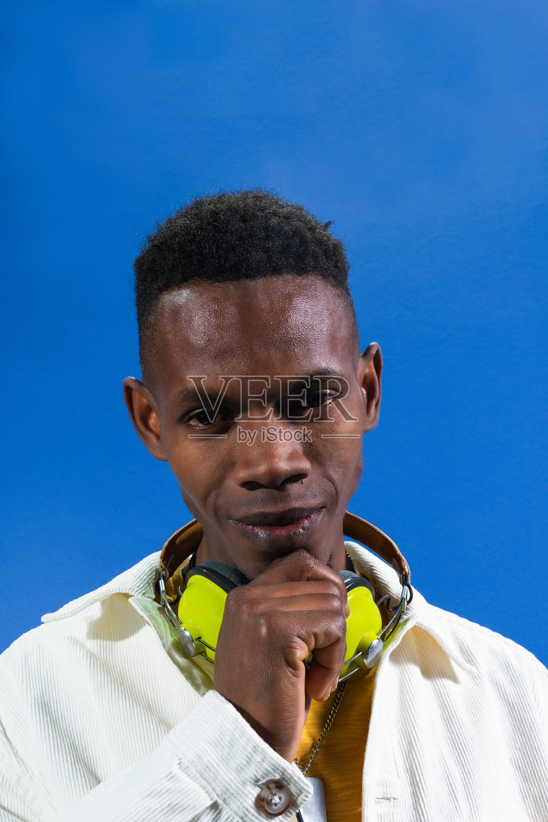 年轻的DJ在蓝色背景下沉思，耳机挂在脖子上照片摄影图片