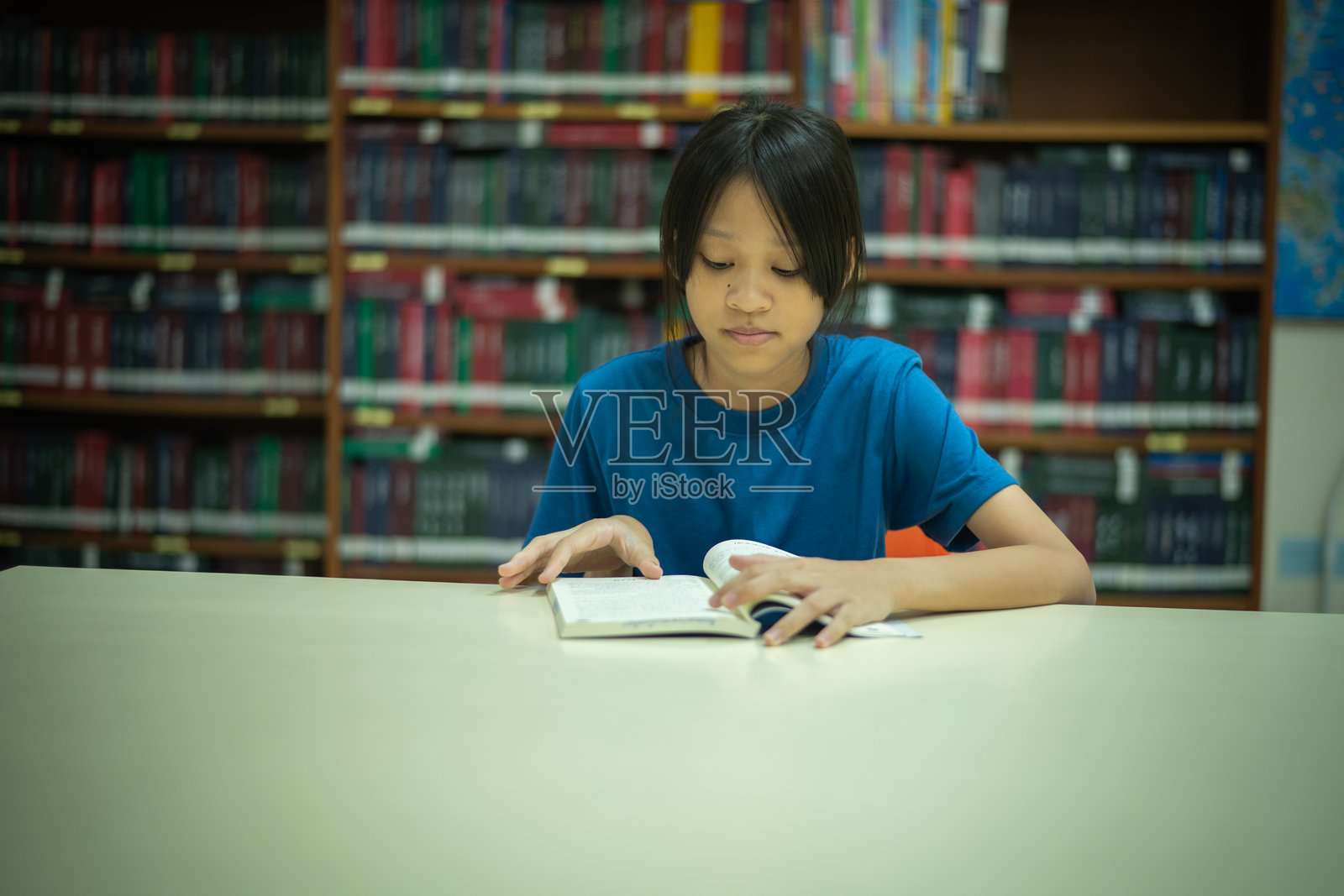 年轻女孩的表情显得平静而专注，暗示着深度的专注。图像的构图平衡，中心位置吸引了观众的注意力，展现了她与书籍和教育环境的互动。照片摄影图片
