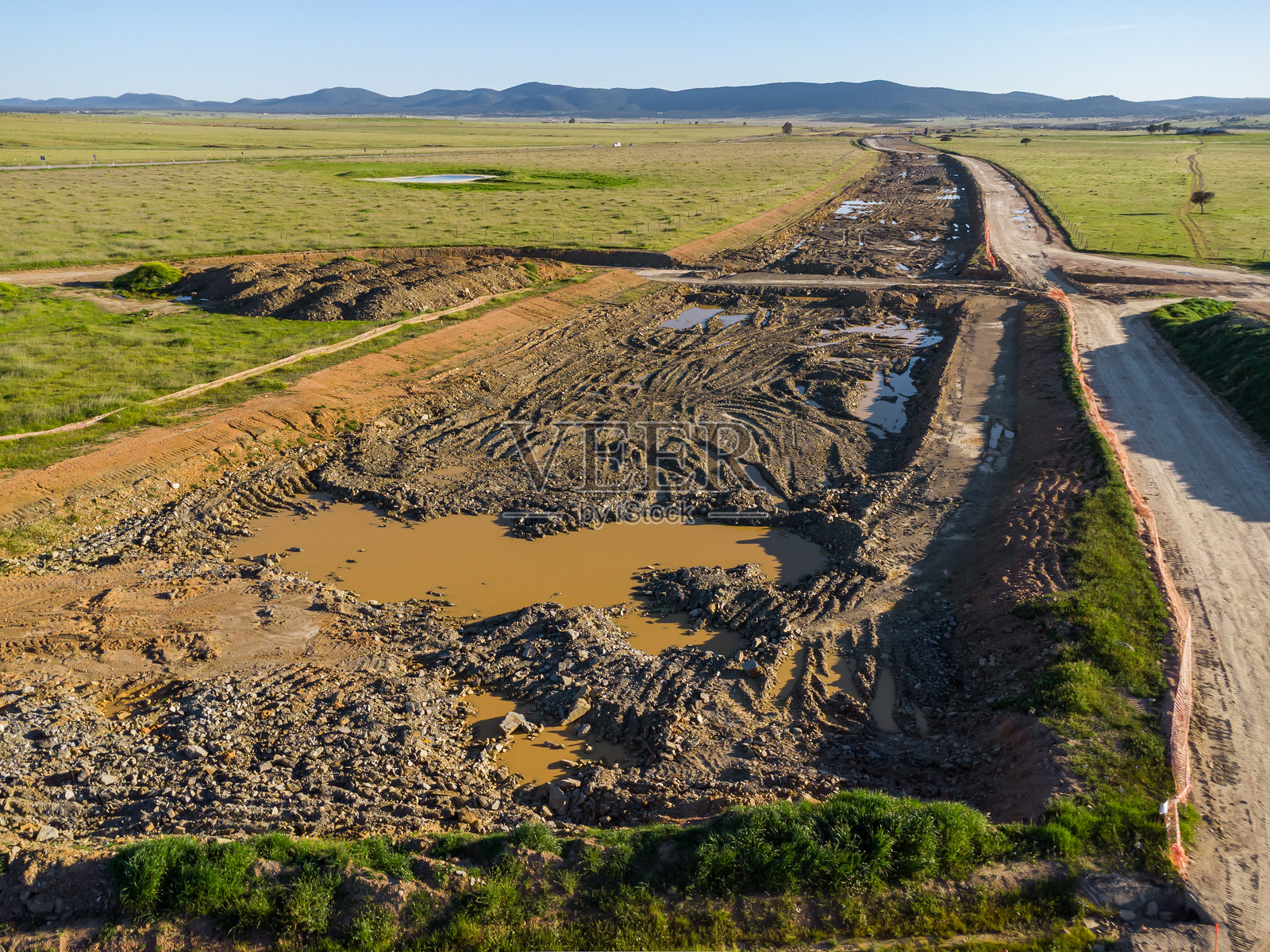 建筑沟渠的鸟瞰图：水满的土方切口蜿蜒向山脉地平线，夕阳下的景色。照片摄影图片
