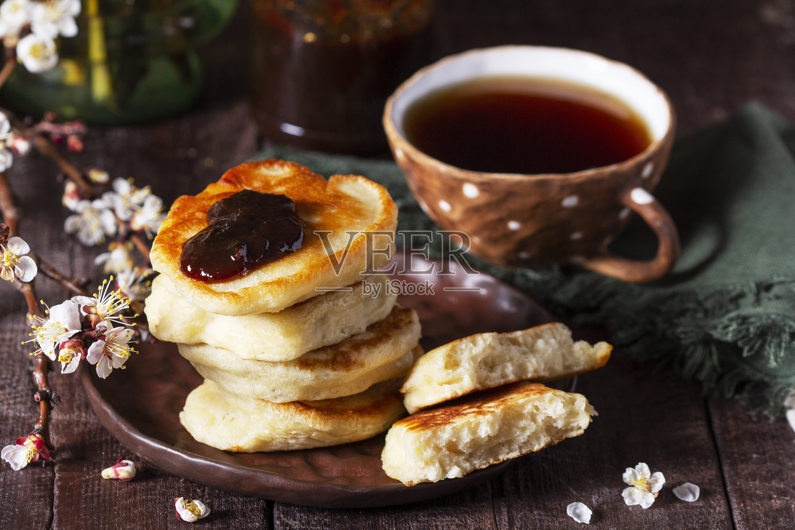复活节酵母煎饼配梅子酱和茶，木桌上摆放着一束盛开的杏树枝。照片摄影图片