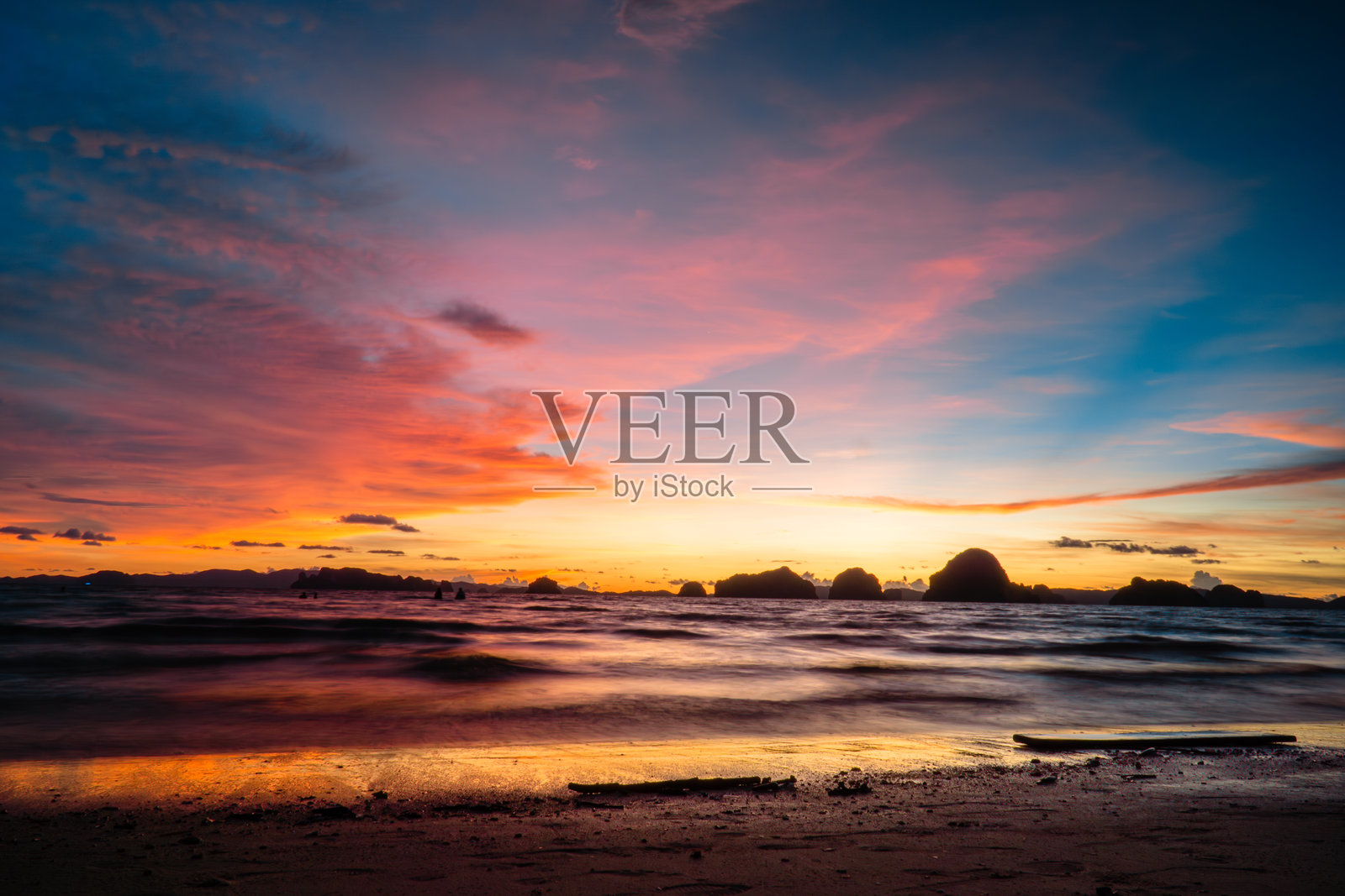 海边的晚霞，波浪拍打着沙滩，天空呈现出多种色彩。照片摄影图片