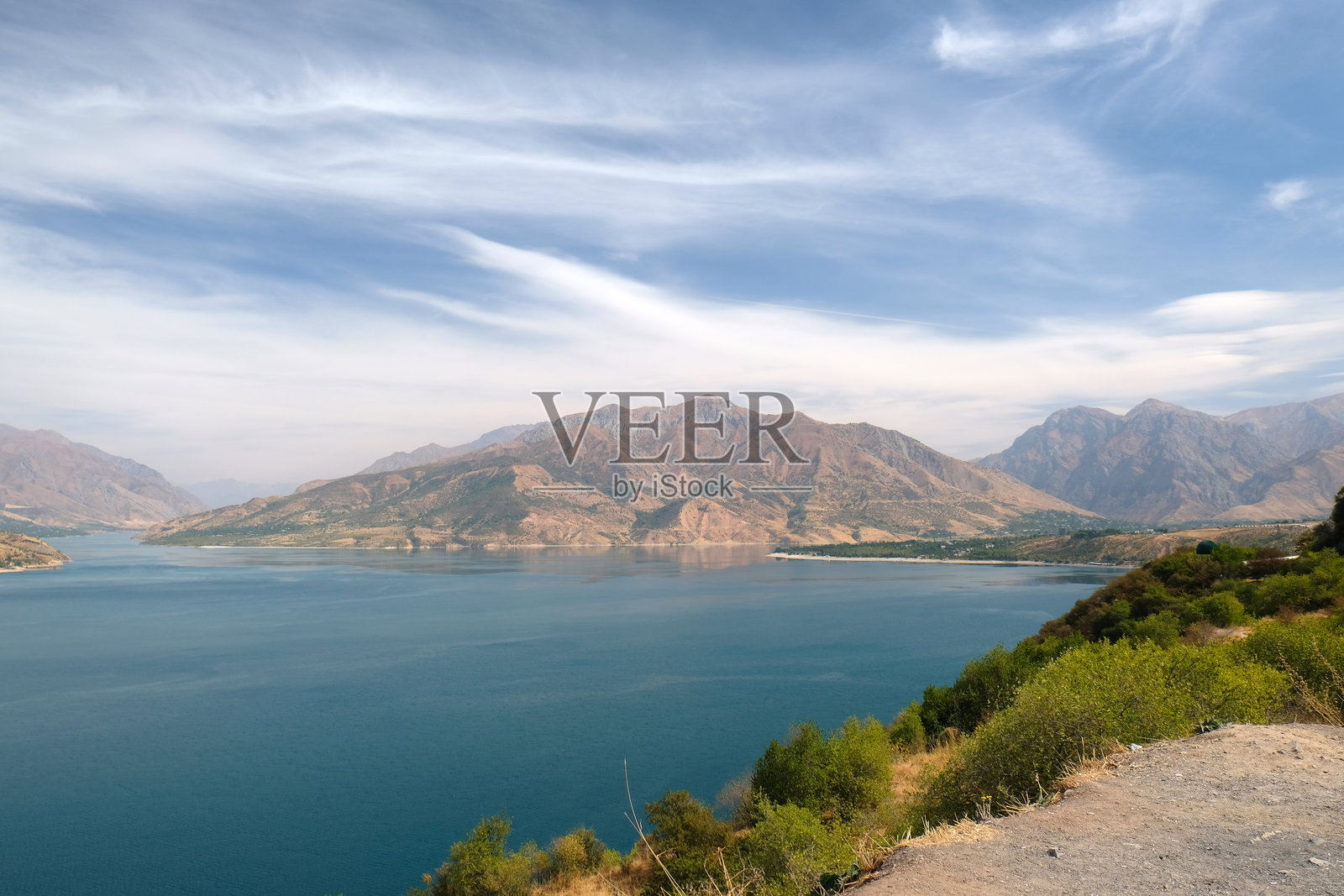 白天晴朗的蓝天下，宁静的湖泊与城市背景相映衬的山地风景。照片摄影图片