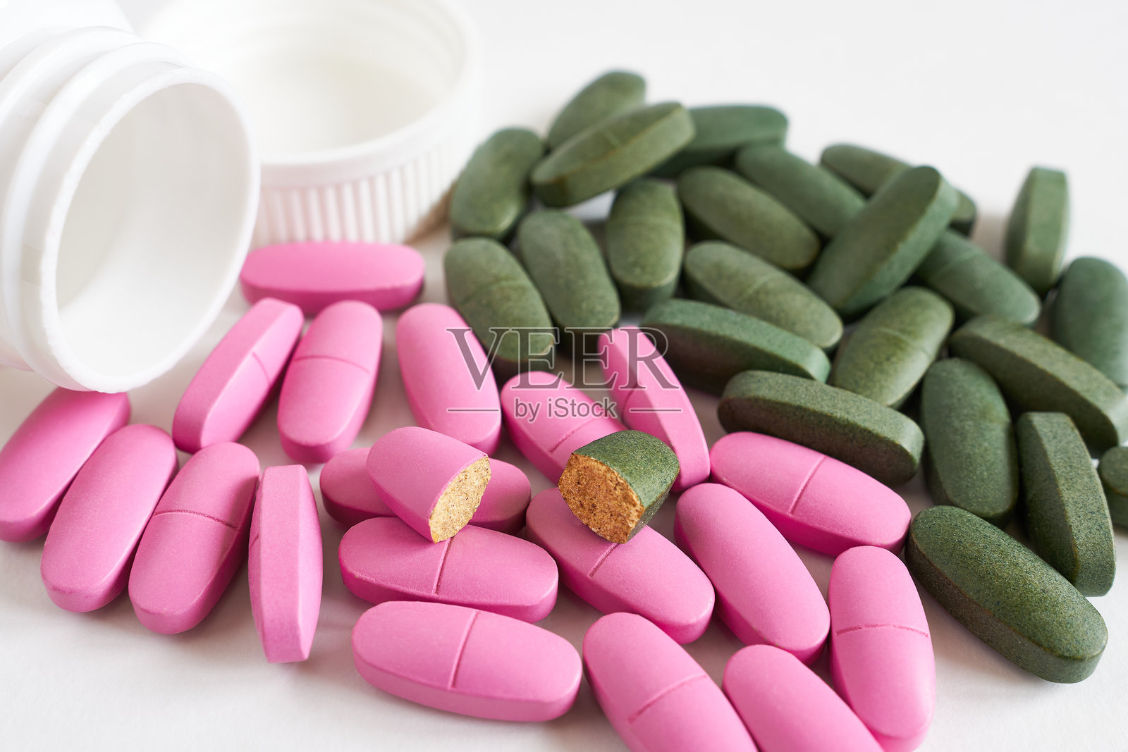 粉色和绿色药丸从药瓶中倾倒出来的特写镜头。照片摄影图片