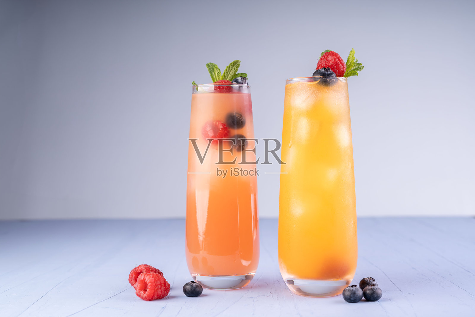 清新的柑橘和浆果鸡尾酒，搭配薄荷装饰，盛在高脚杯中，背景简约，突出鲜艳的橙色和粉色，周围散落着新鲜的覆盆子和蓝莓。照片摄影图片