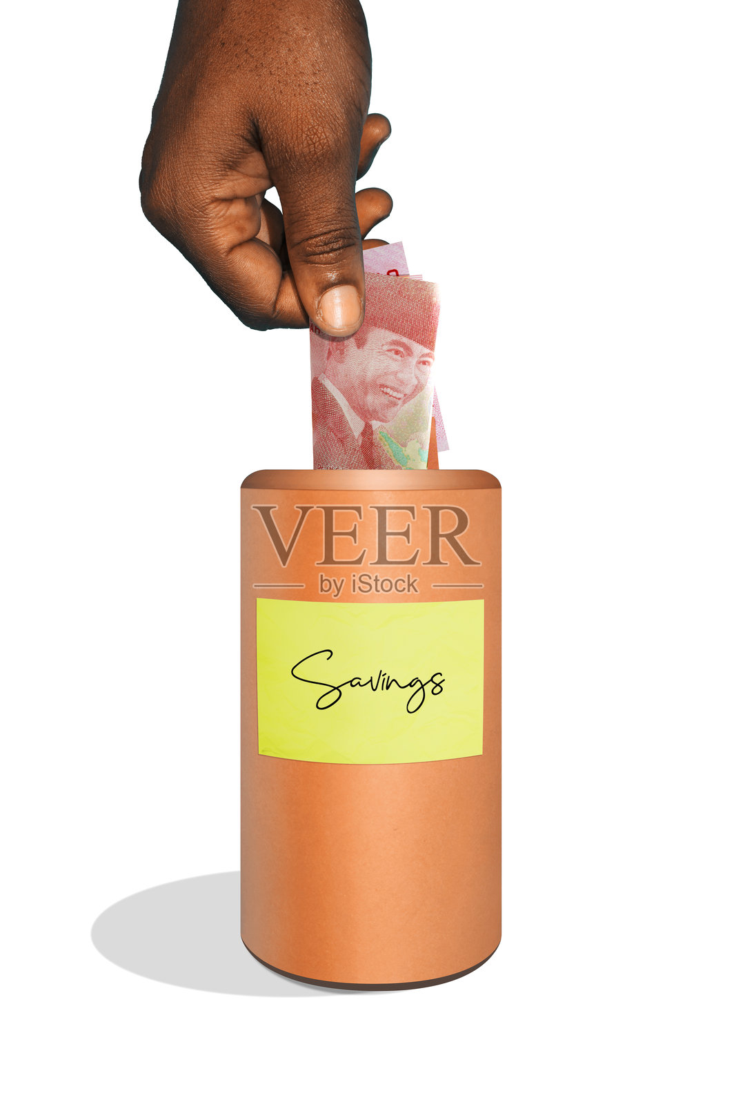 黑手将100000印尼盾纸币放入带标签的米色棕色木质圆柱形储蓄箱，背景为白色，个人未来投资，存钱照片摄影图片