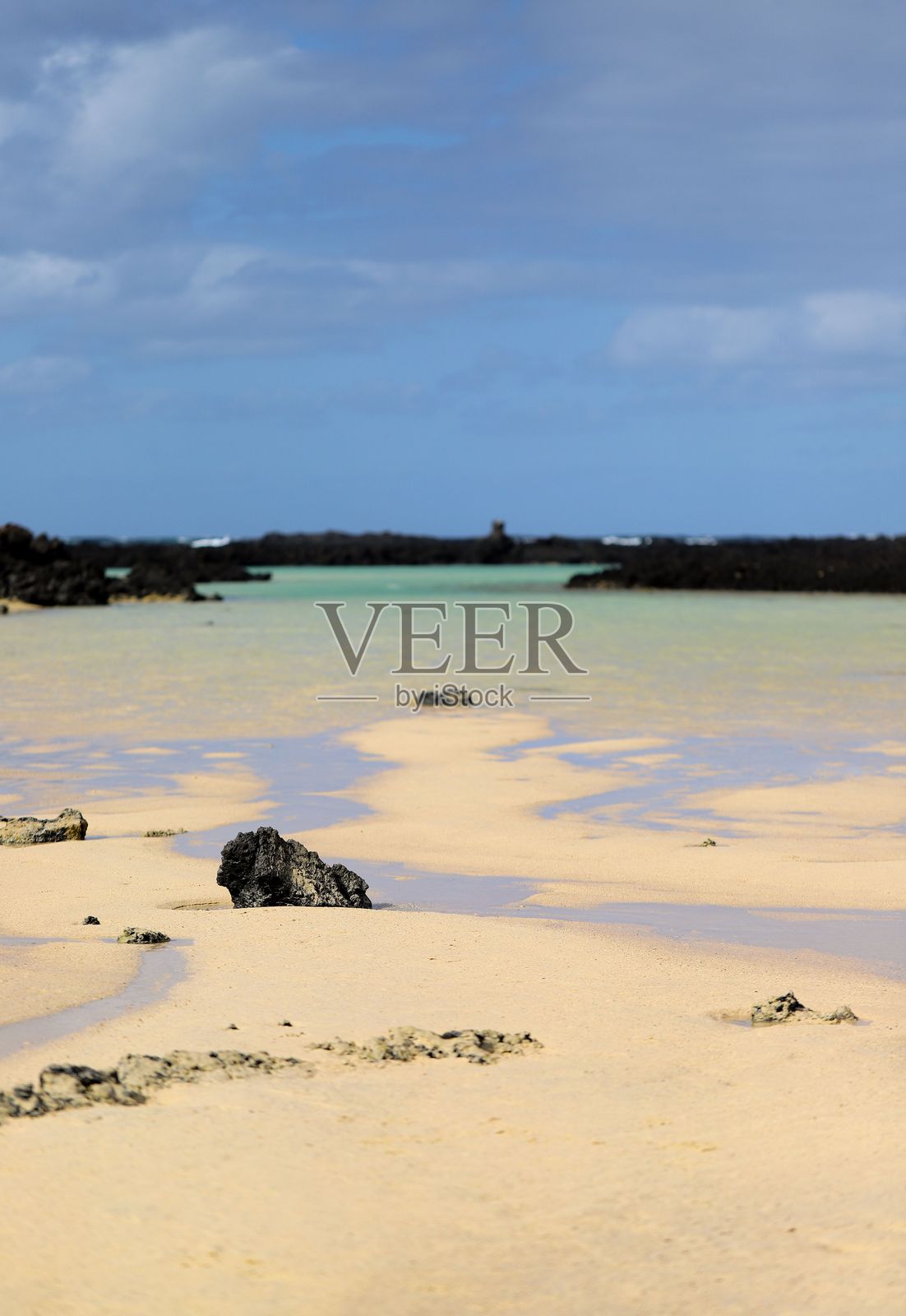 宁静的海滩，金色的沙滩和黑色的岩石。照片摄影图片