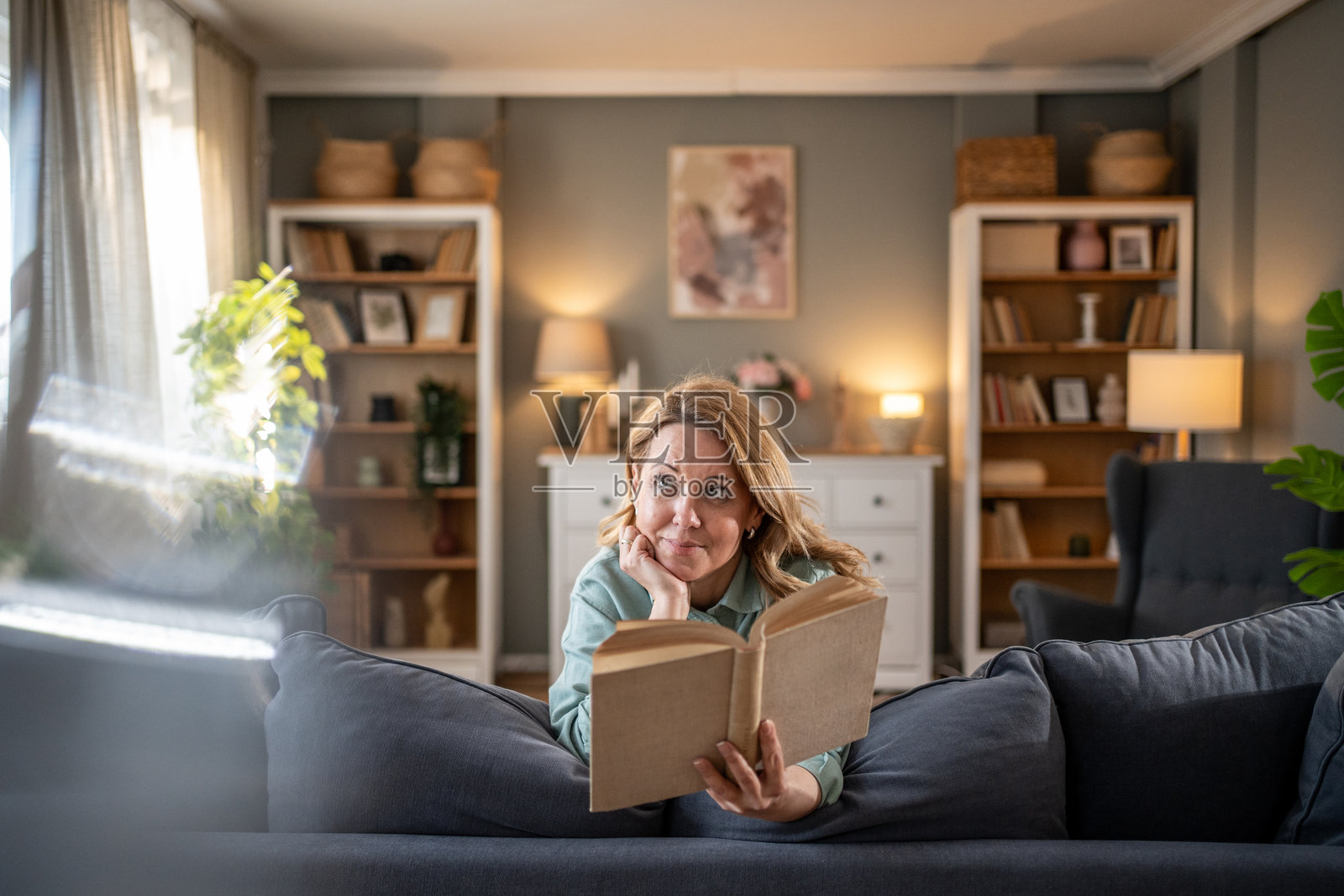 中年女性在沙发上放松，阅读一本书并做白日梦照片摄影图片
