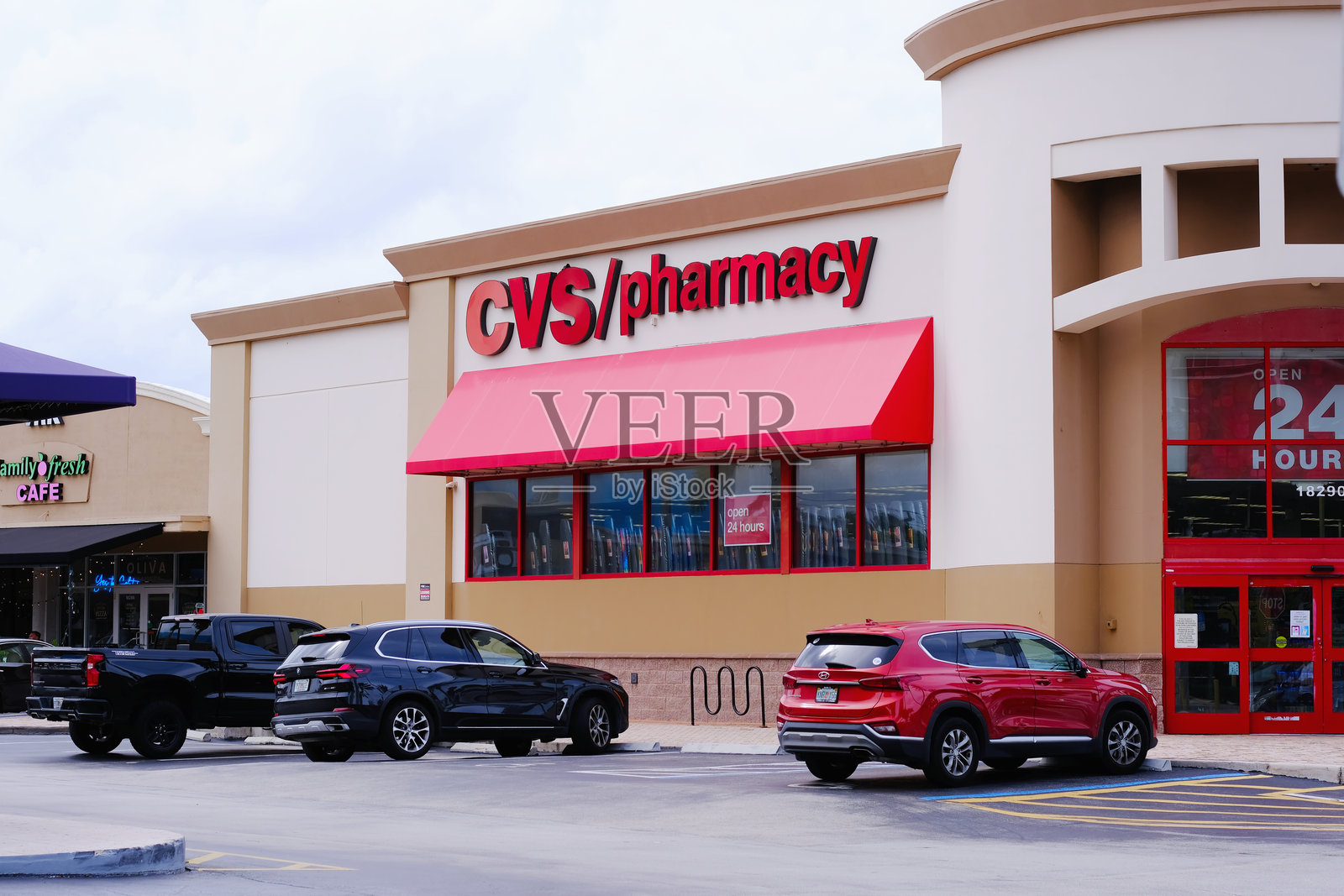 CVS药店外观，醒目的红色标志，大红色遮阳篷，入口附近停着的汽车，广告显示24小时营业。照片摄影图片
